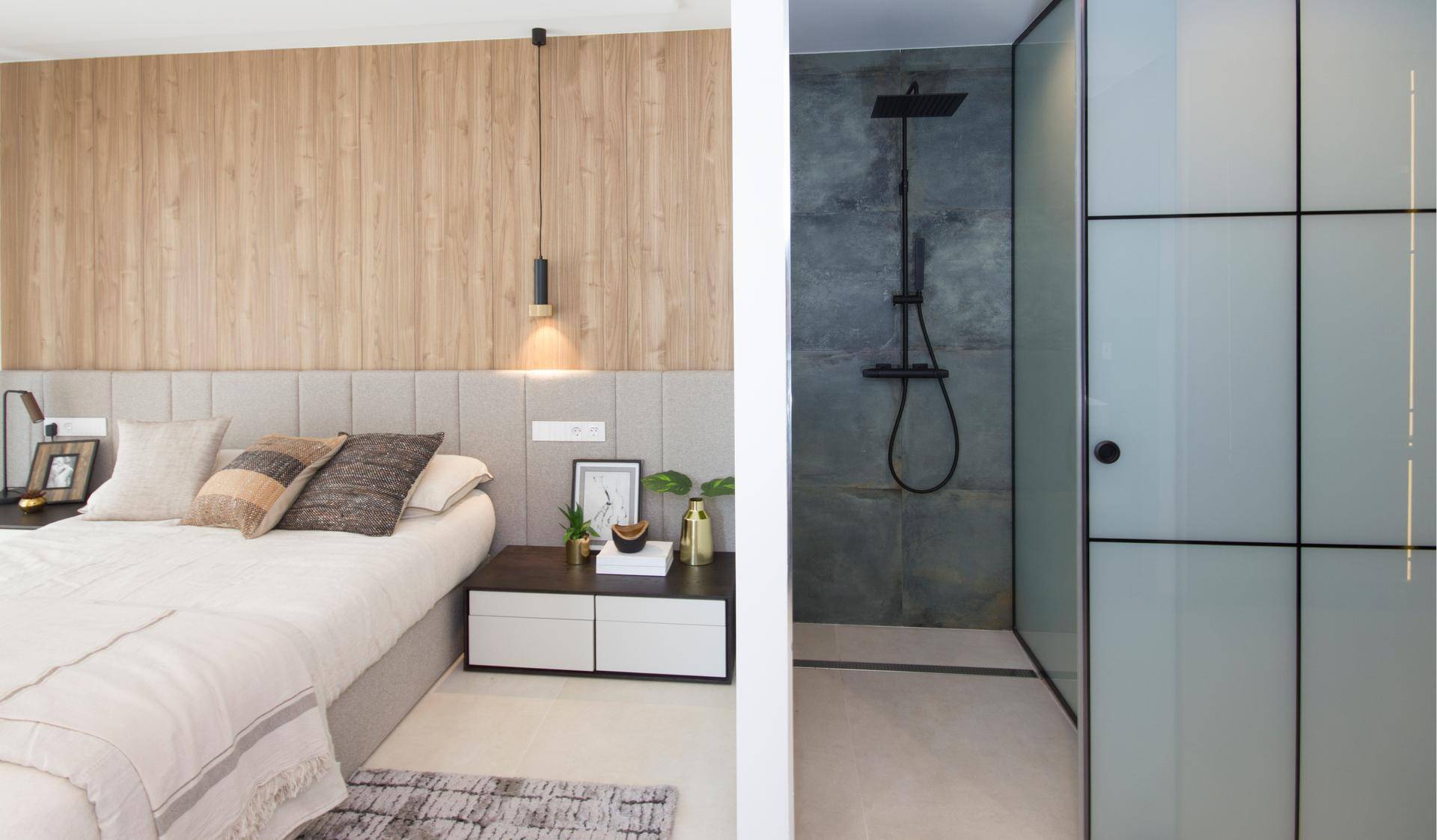 Schlafzimmer mit Holzwand und angrenzender moderner Dusche mit Glasabtrennung.