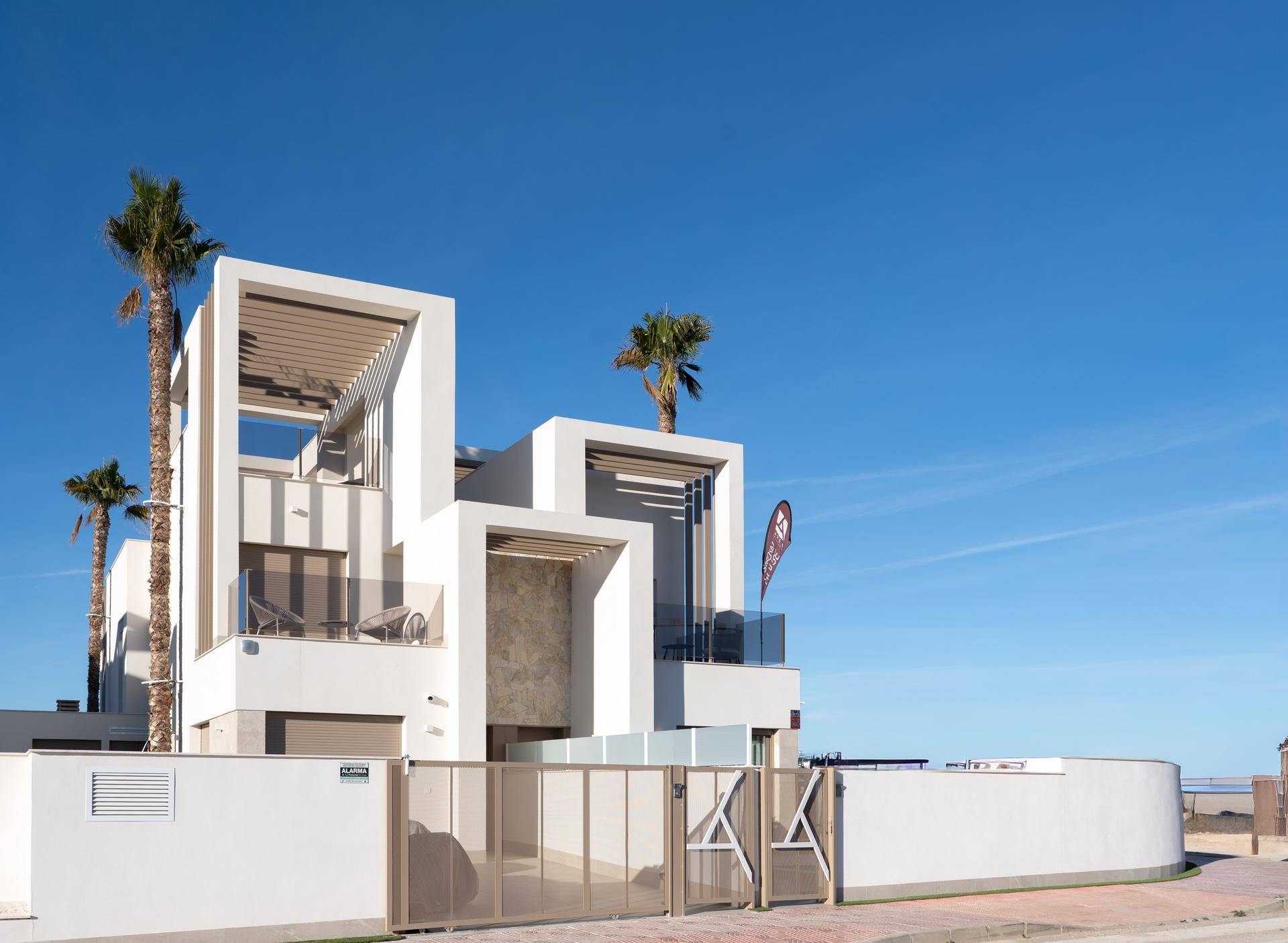 Moderne weiße Villa mit klaren Linien, Balkonen und Palmen unter strahlend blauem Himmel.