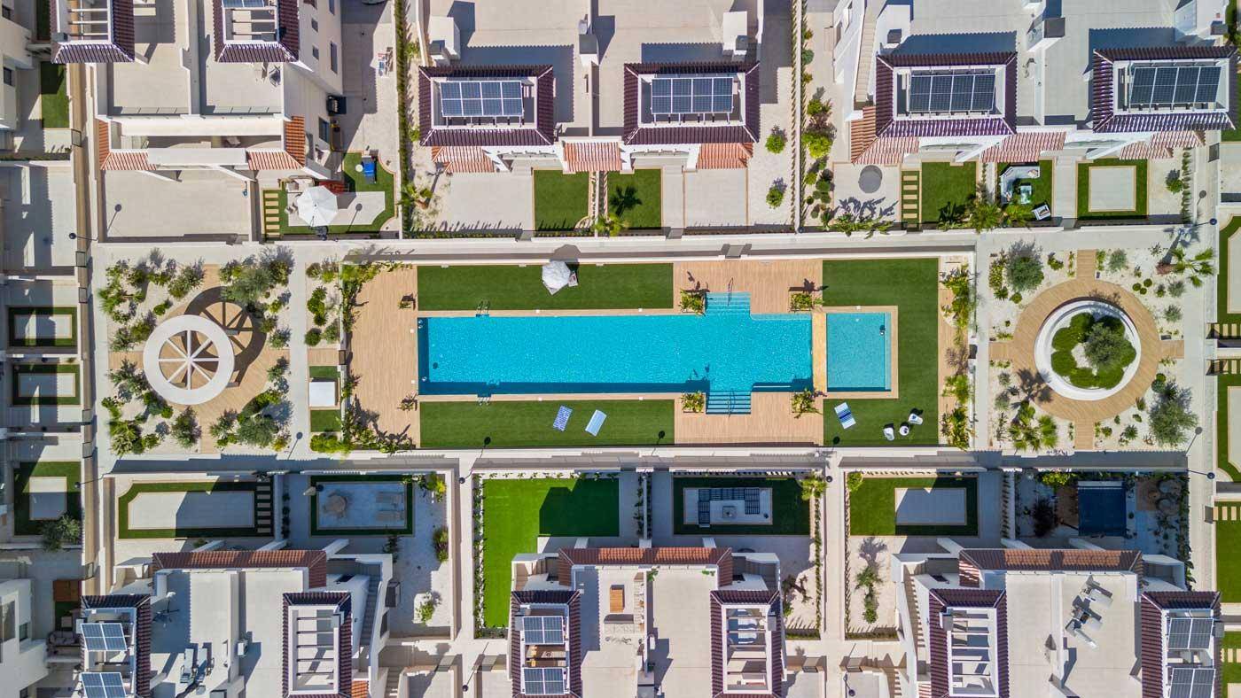 Luftaufnahme der Wohnanlage mit zentraler Poollandschaft und Solaranlagen auf den Dächern.