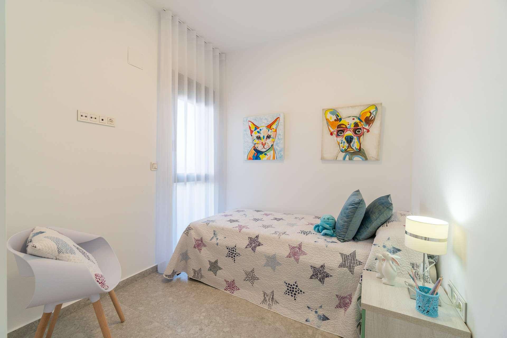 Helles Schlafzimmer mit Einzelbett, weißer Einrichtung und farbenfrohen Tierbildern an der Wand.