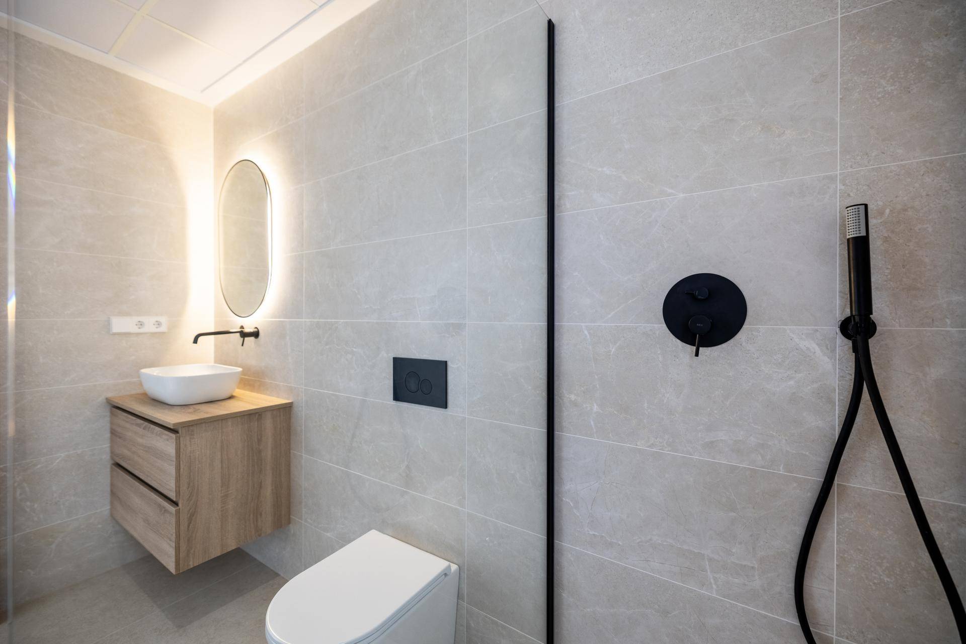 Modernes Badezimmer mit schwebendem Waschtisch, beleuchtetem Spiegel und begehbarer Dusche.