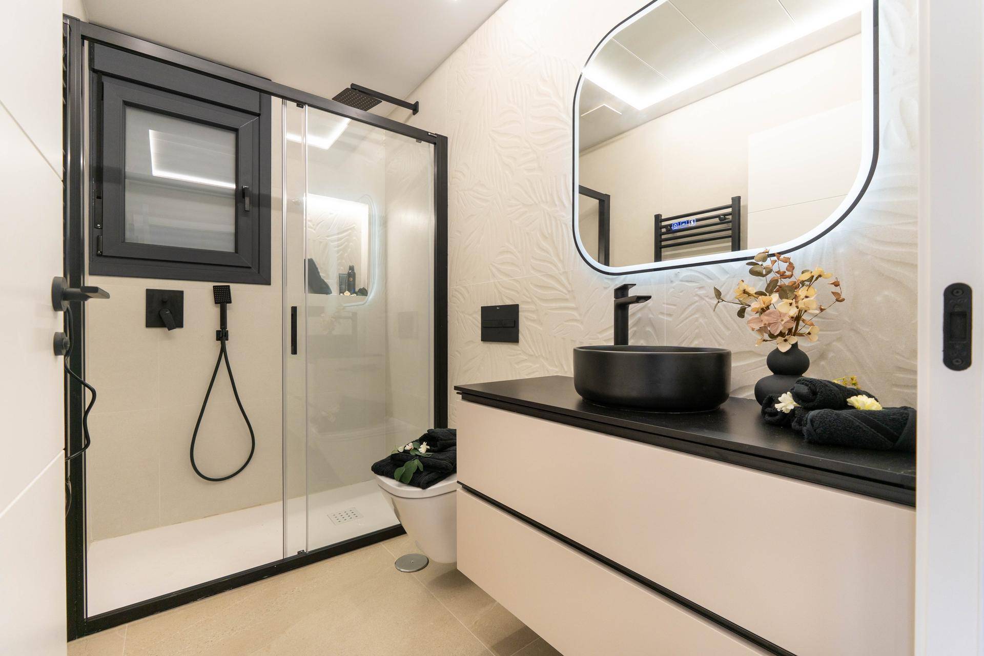 Elegantes Badezimmer mit begehbarer Dusche, schwarzem Waschbecken und beleuchtetem Spiegel.