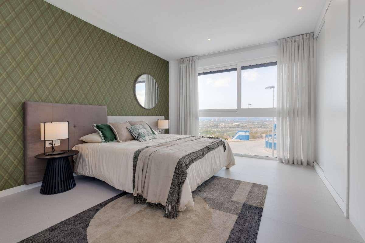 Modernes Schlafzimmer mit grüner Akzentwand, großem Fenster und Blick auf die Umgebung.