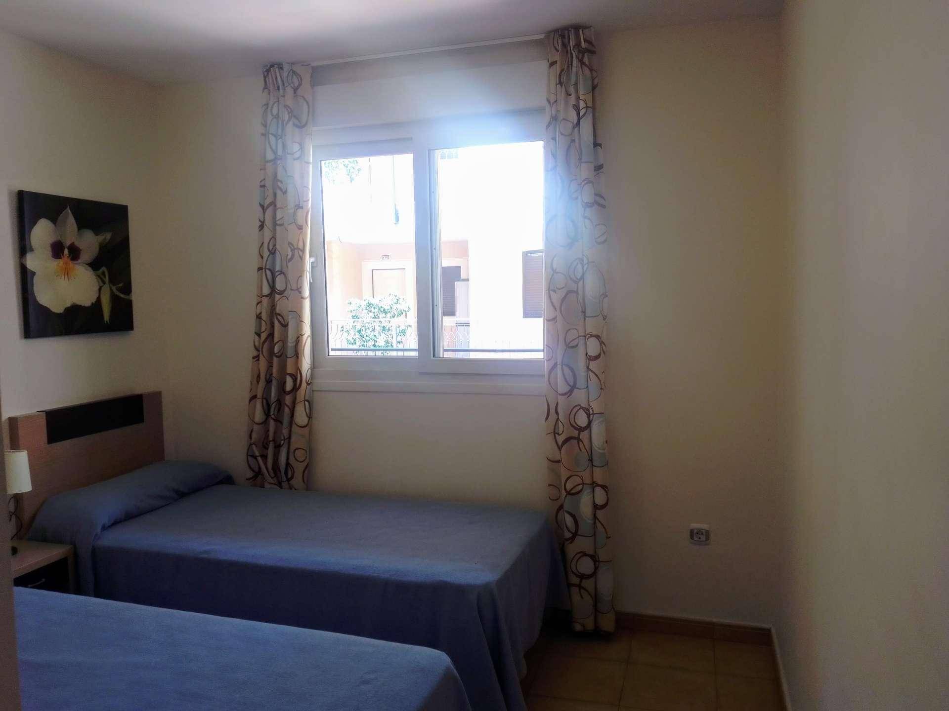 Schlafzimmer mit zwei Einzelbetten, Fliesenboden und einem Fenster mit Vorhängen.