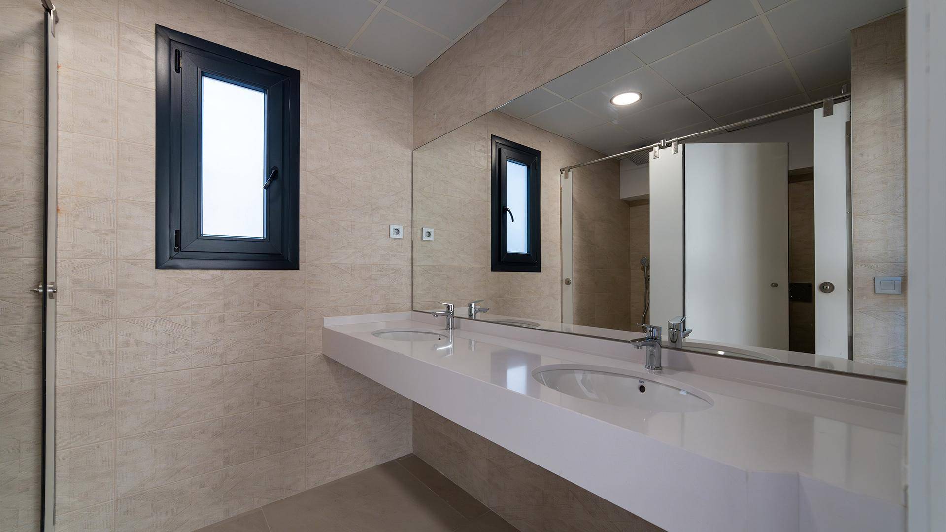 Geräumiges Badezimmer mit Doppelwaschtisch, großem Spiegel und Fenster.
