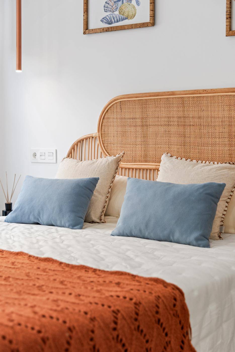 Gemütliches Schlafzimmer mit Rattan-Kopfteil, blauen Kissen und warmer Decke.