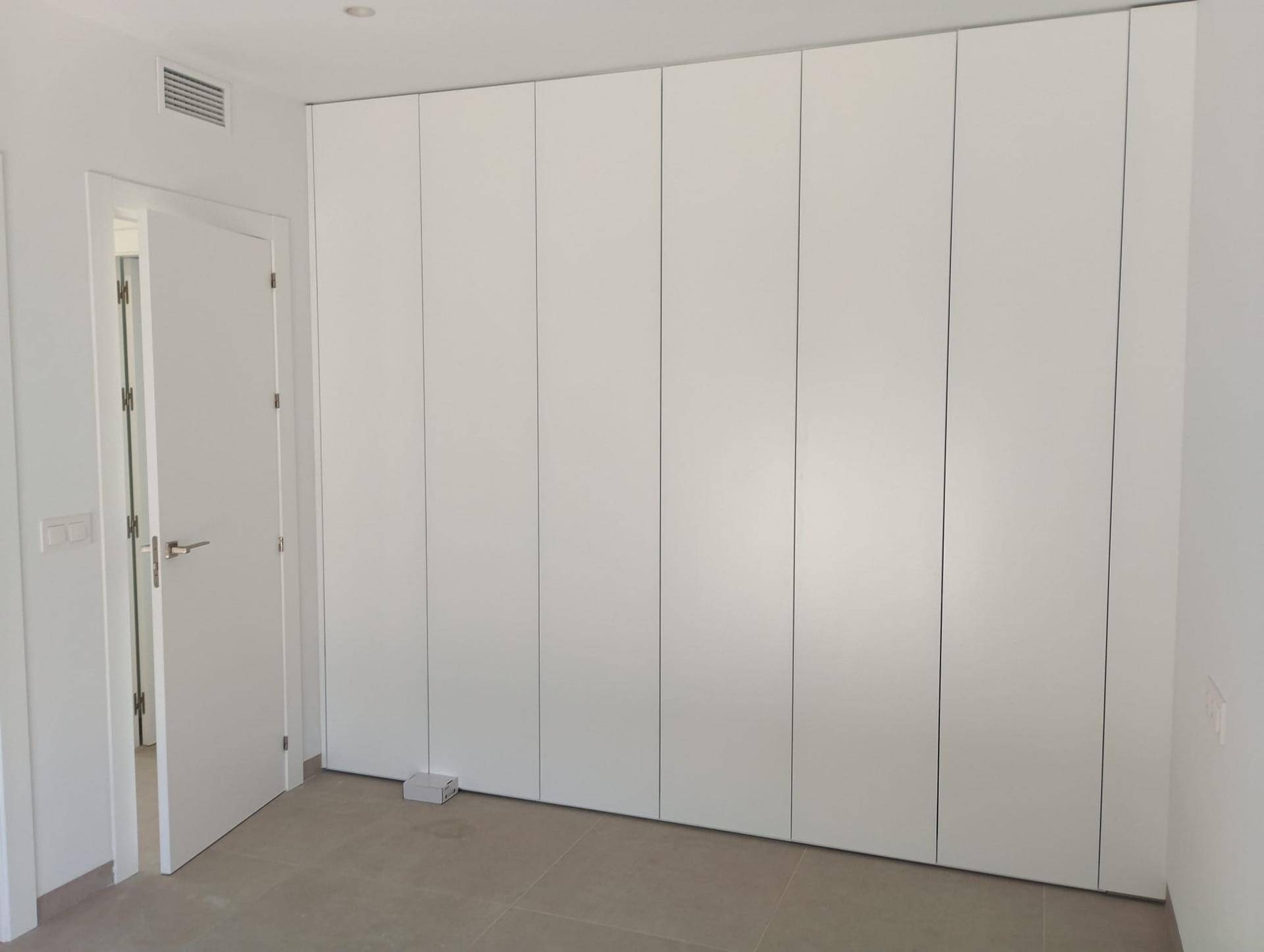 Geräumiger Einbauschrank mit weißen Türen und viel Stauraum in einem hellen Zimmer.
