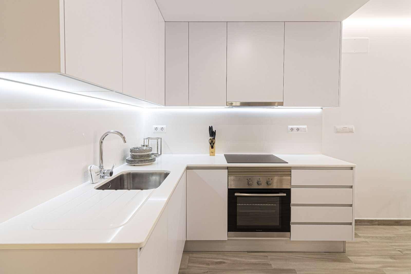 Moderne weiße Einbauküche mit Induktionskochfeld, Backofen und integrierter Beleuchtung.
