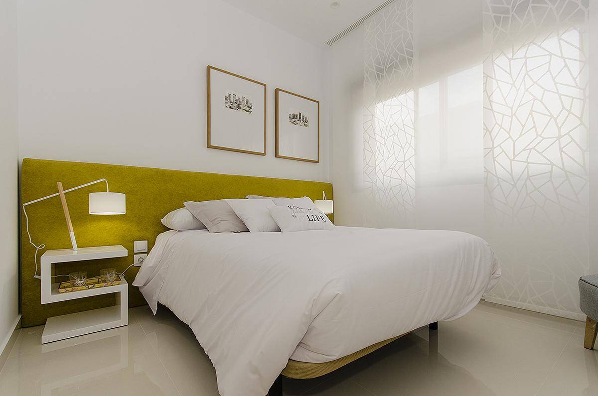 Modernes Schlafzimmer mit Doppelbett, gelbem Akzent und viel natürlichem Licht.