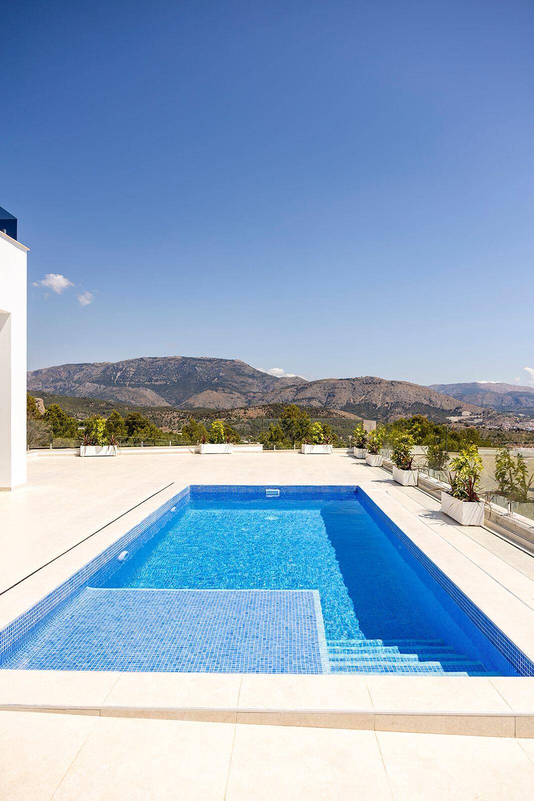 Großer Poolbereich mit blauen Mosaikfliesen und weitem Panoramablick auf die Berge.