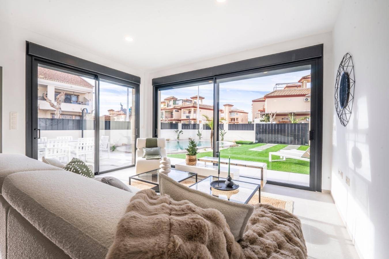 Komfortables Wohnzimmer mit großem Sofa und weitem Blick durch die Glasschiebetüren auf den Pool und Garten.