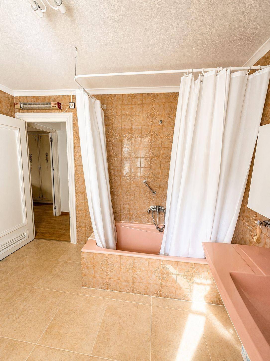 Badezimmer im Stil der 80er Jahre mit rosa Badewanne, beigen Fliesen und Duschvorhang.