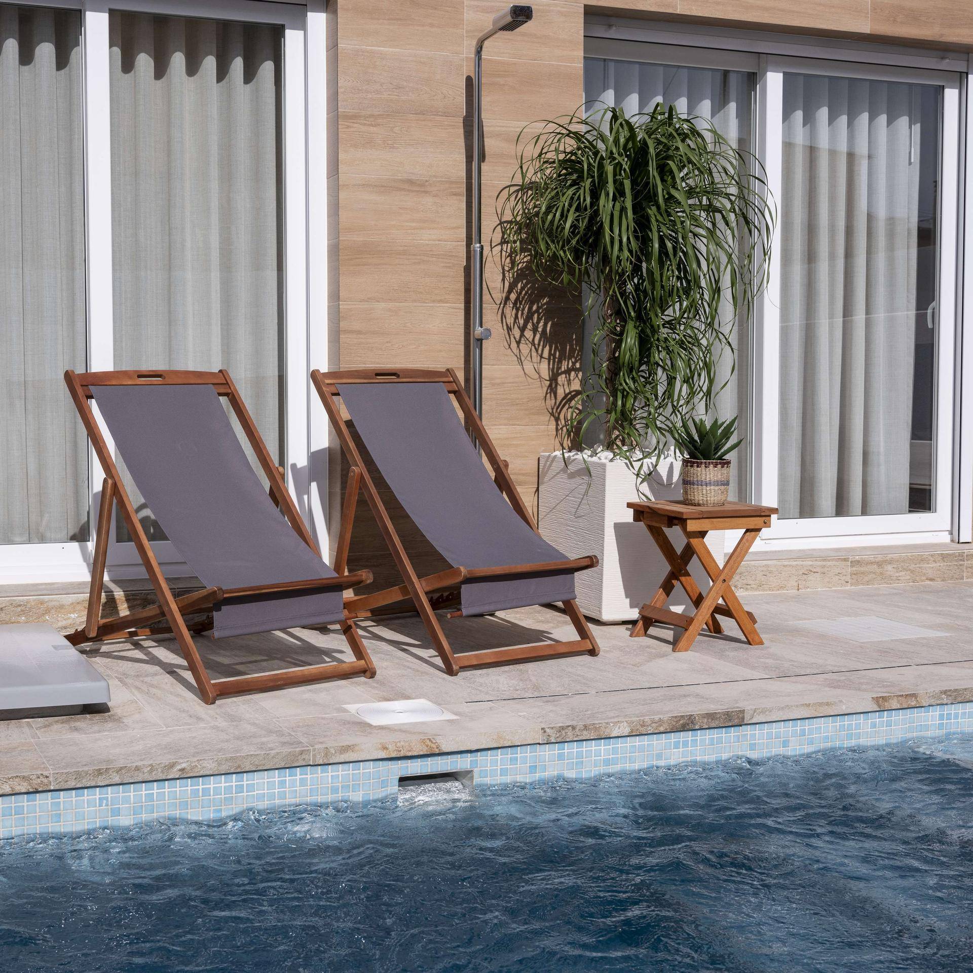 Detailansicht des Pools mit blauen Mosaikfliesen und bequemen Liegestühlen auf der Terrasse.