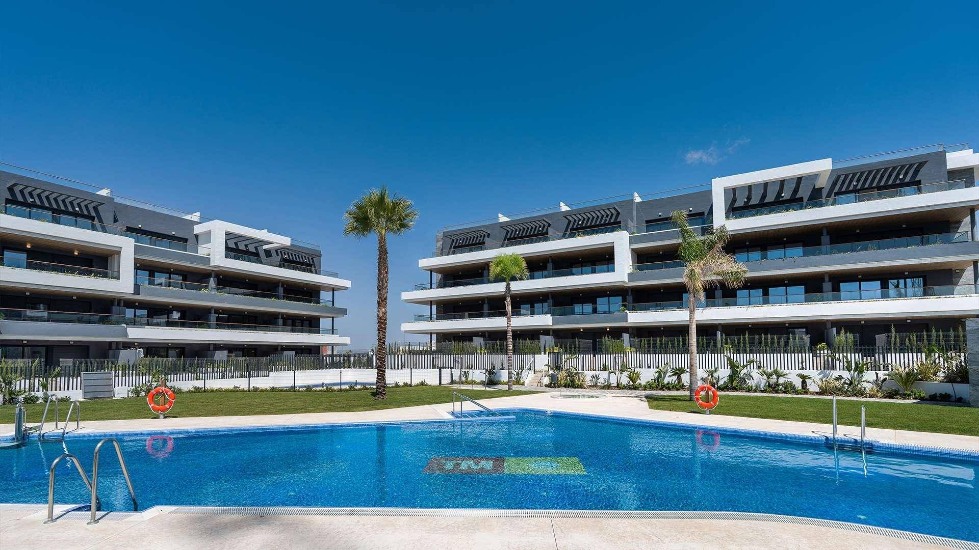 Moderne Wohnanlage mit großem Gemeinschaftspool und weitläufigen Grünflächen unter blauem Himmel.