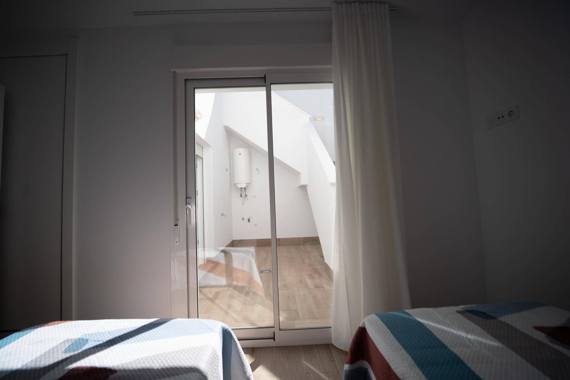 Schlafzimmer mit Schiebetür, die zu einem hellen Außenbereich oder Treppenhaus führt.