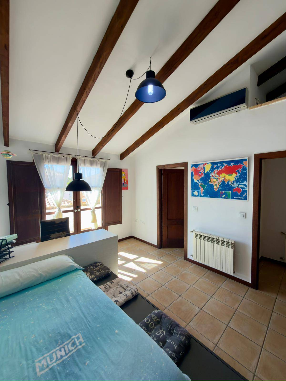 Schlafzimmer mit Holzbalken, Klimaanlage, Heizkörper und Weltkarte an der Wand.