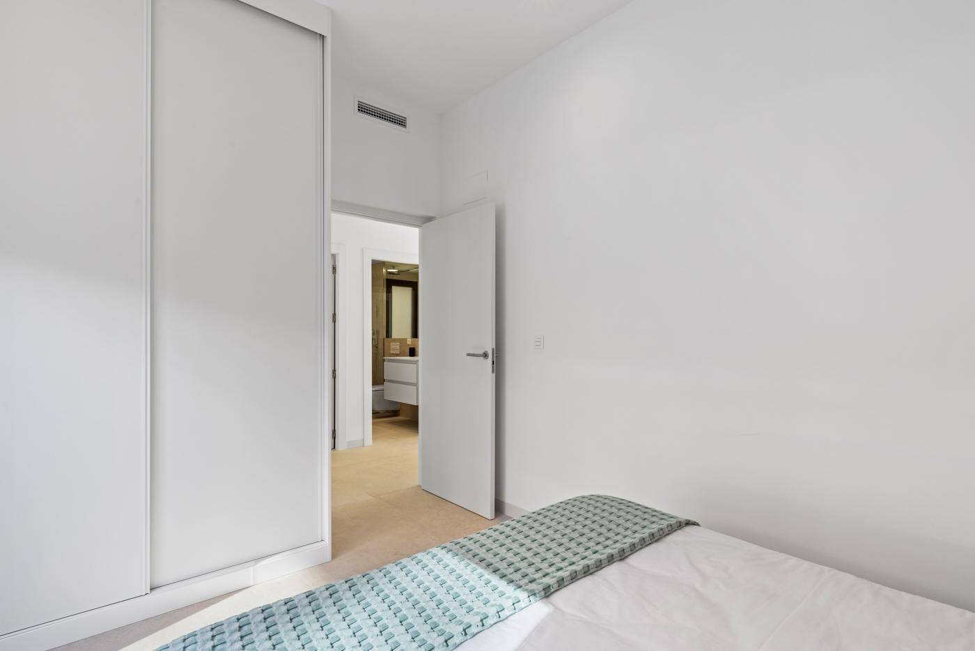 Schlafzimmer mit integrierten Schränken und Zugang zu einem modernen Badezimmer.