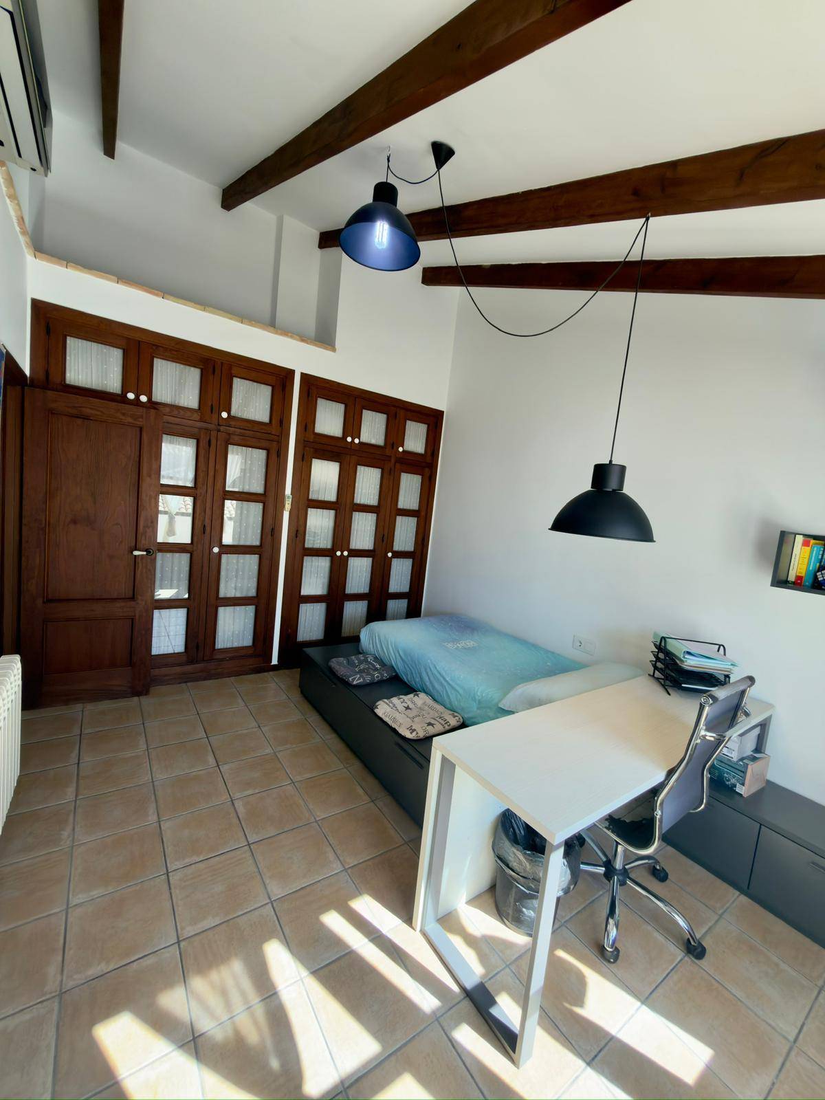 Schlafzimmer mit sichtbaren Holzbalken, Schreibtisch und modernem Hängesessel.