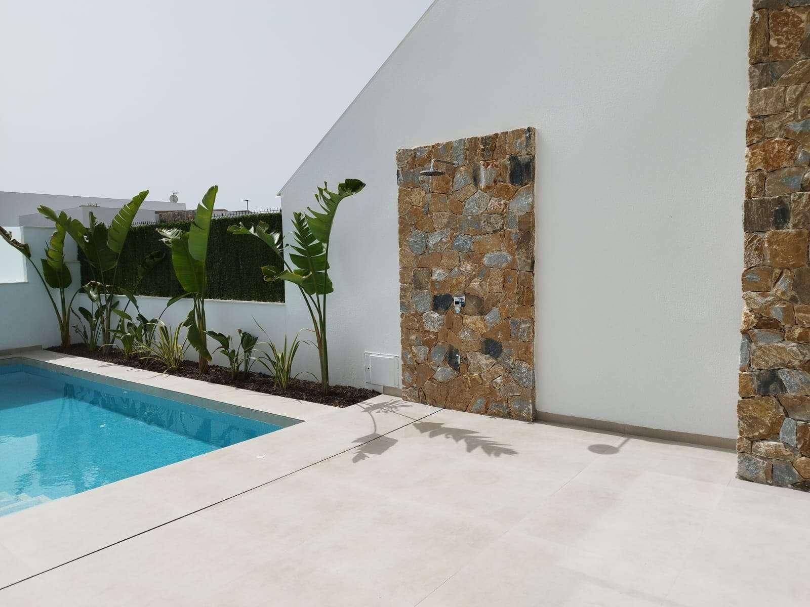 Außenbereich mit Pool, Steindusche und mediterraner Bepflanzung unter strahlendem Himmel.