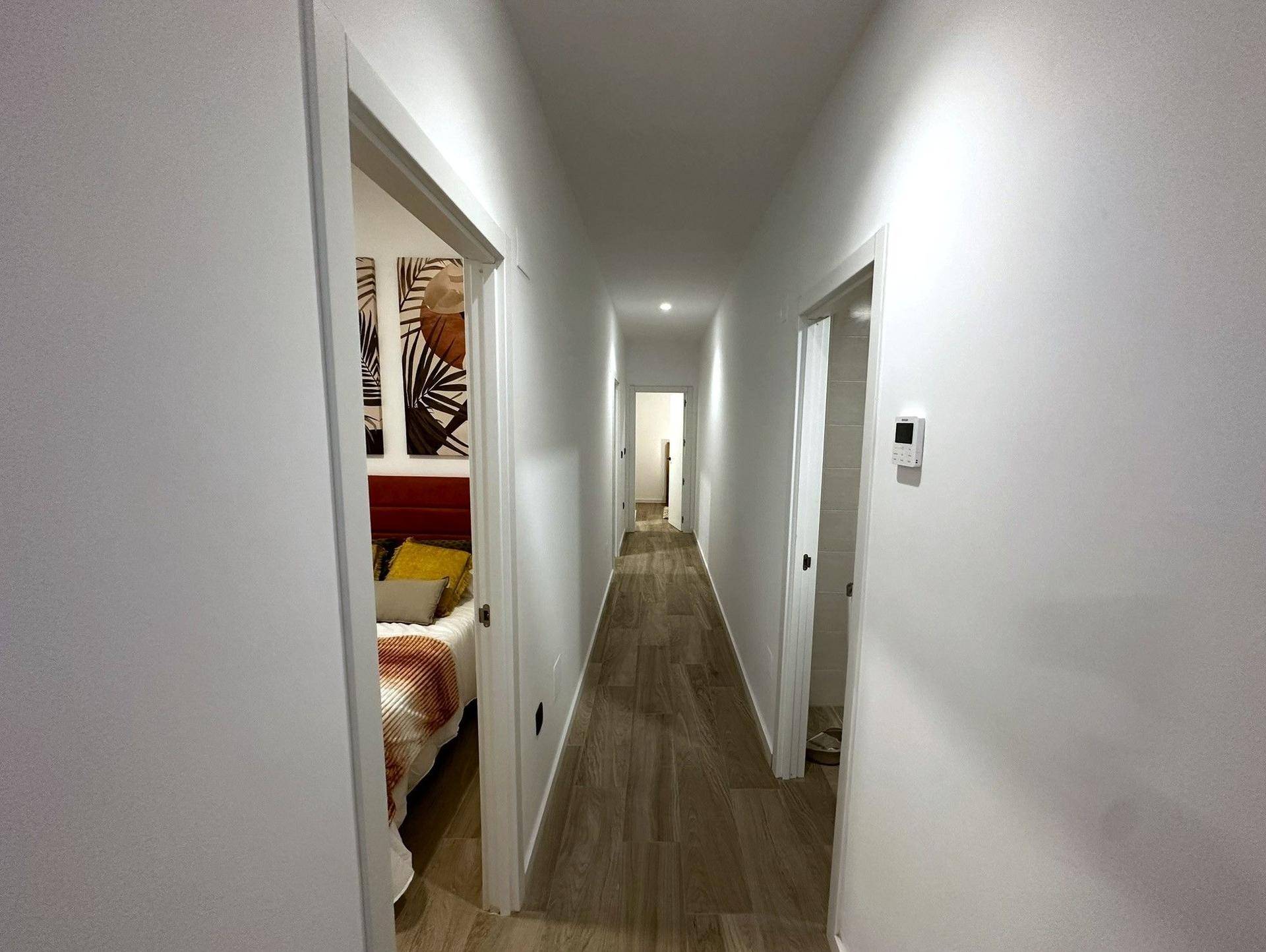 Heller Flur mit modernen Fliesen in Holzoptik und weißen Wänden, der zu weiteren Räumen führt.