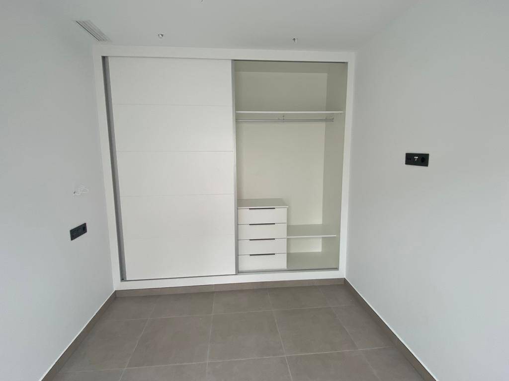 Geräumiger Einbauschrank mit Schiebetüren, Regalen und Schubladen in einem hellen Zimmer.