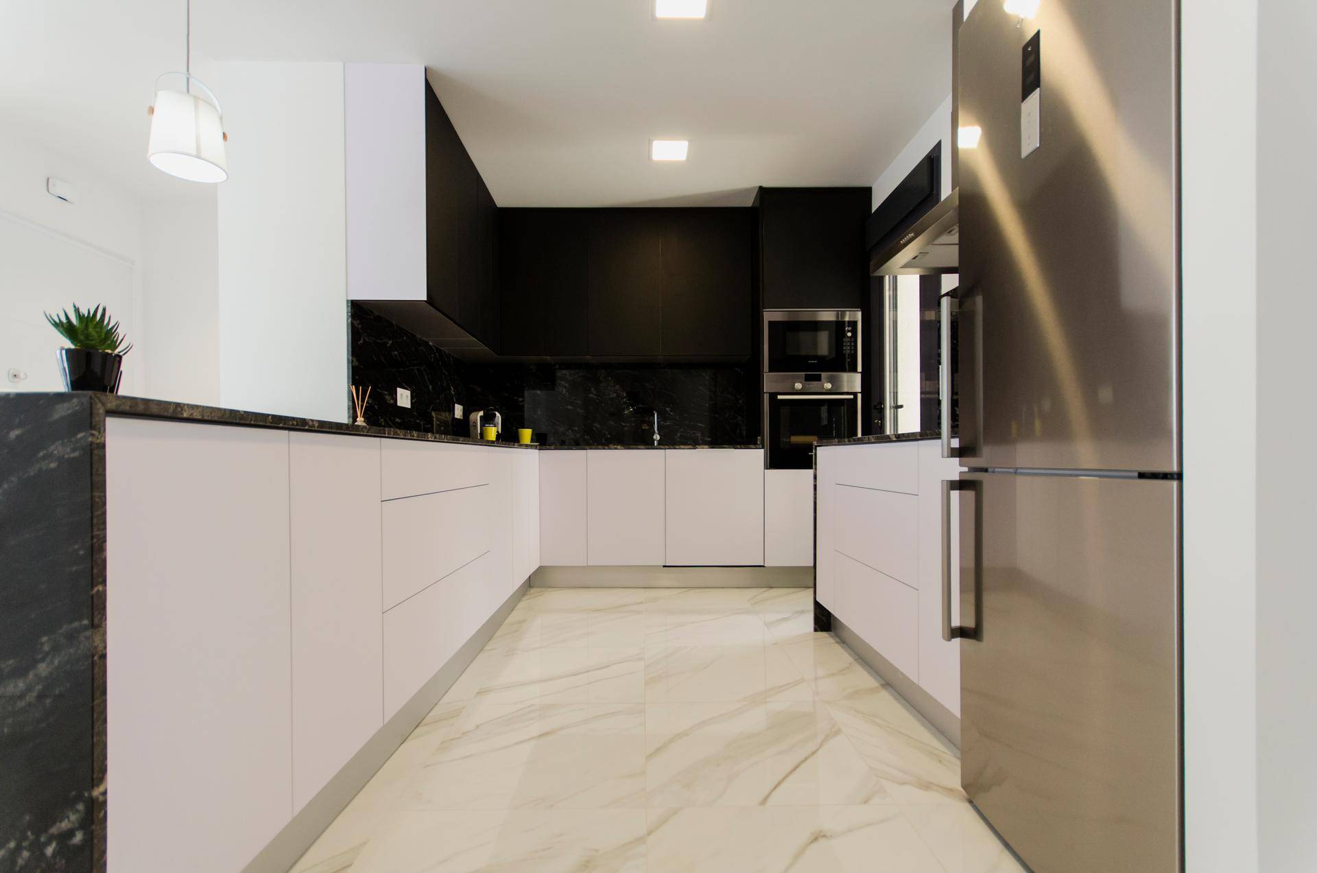 Geräumige moderne Küche mit weißen Unterschränken, schwarzer Granit-Arbeitsplatte und Marmorboden.