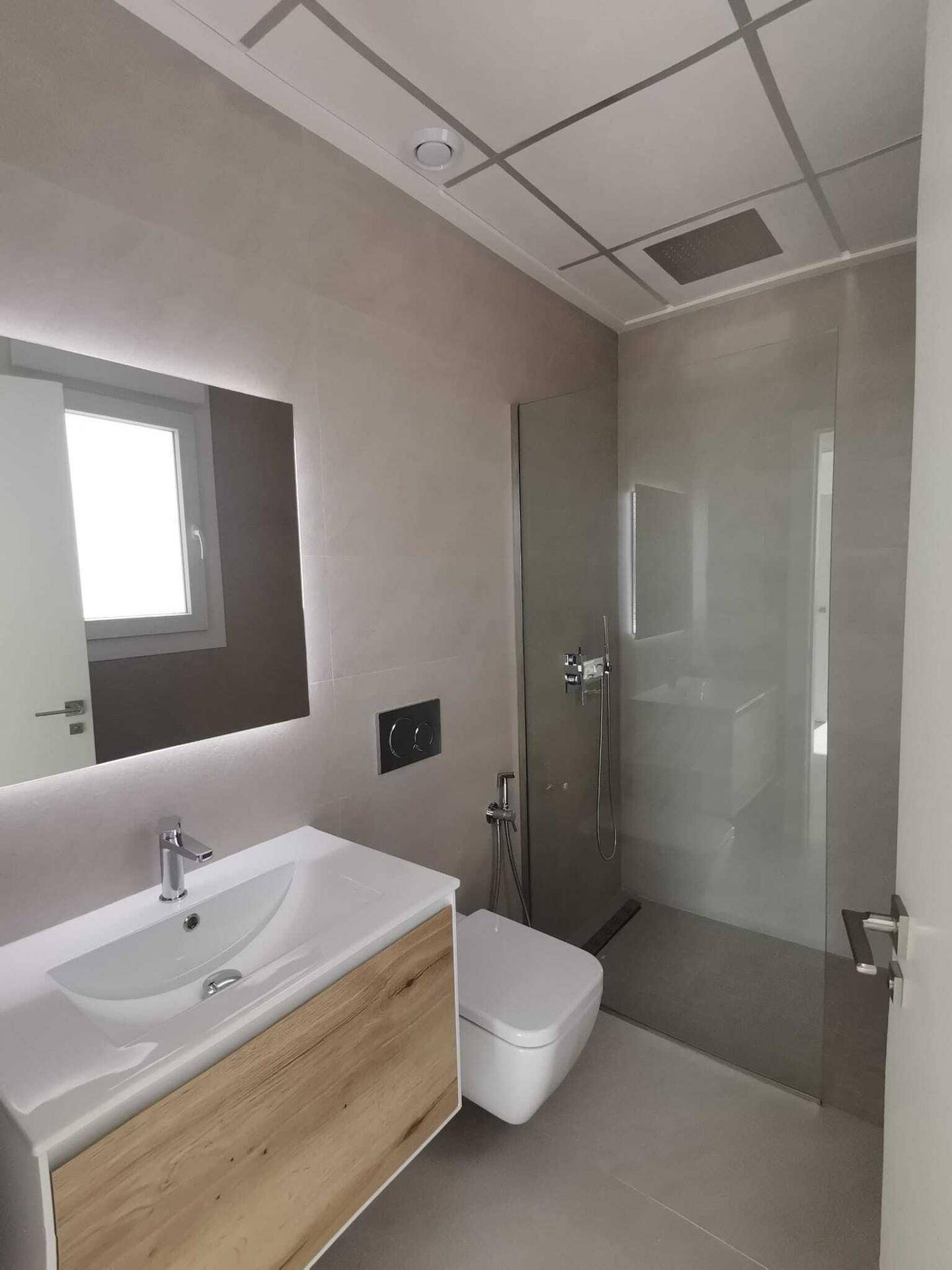 Modernes Badezimmer mit begehbarer Dusche, schwebendem Waschtisch und beleuchtetem Spiegel.