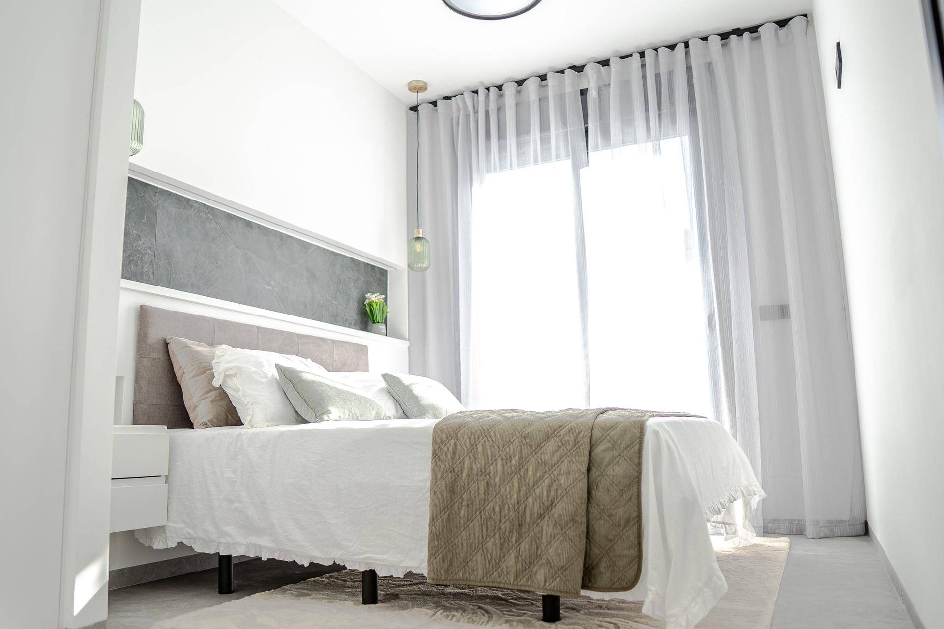 Helles Schlafzimmer mit Doppelbett, Nachttischen und großen Fenstern.