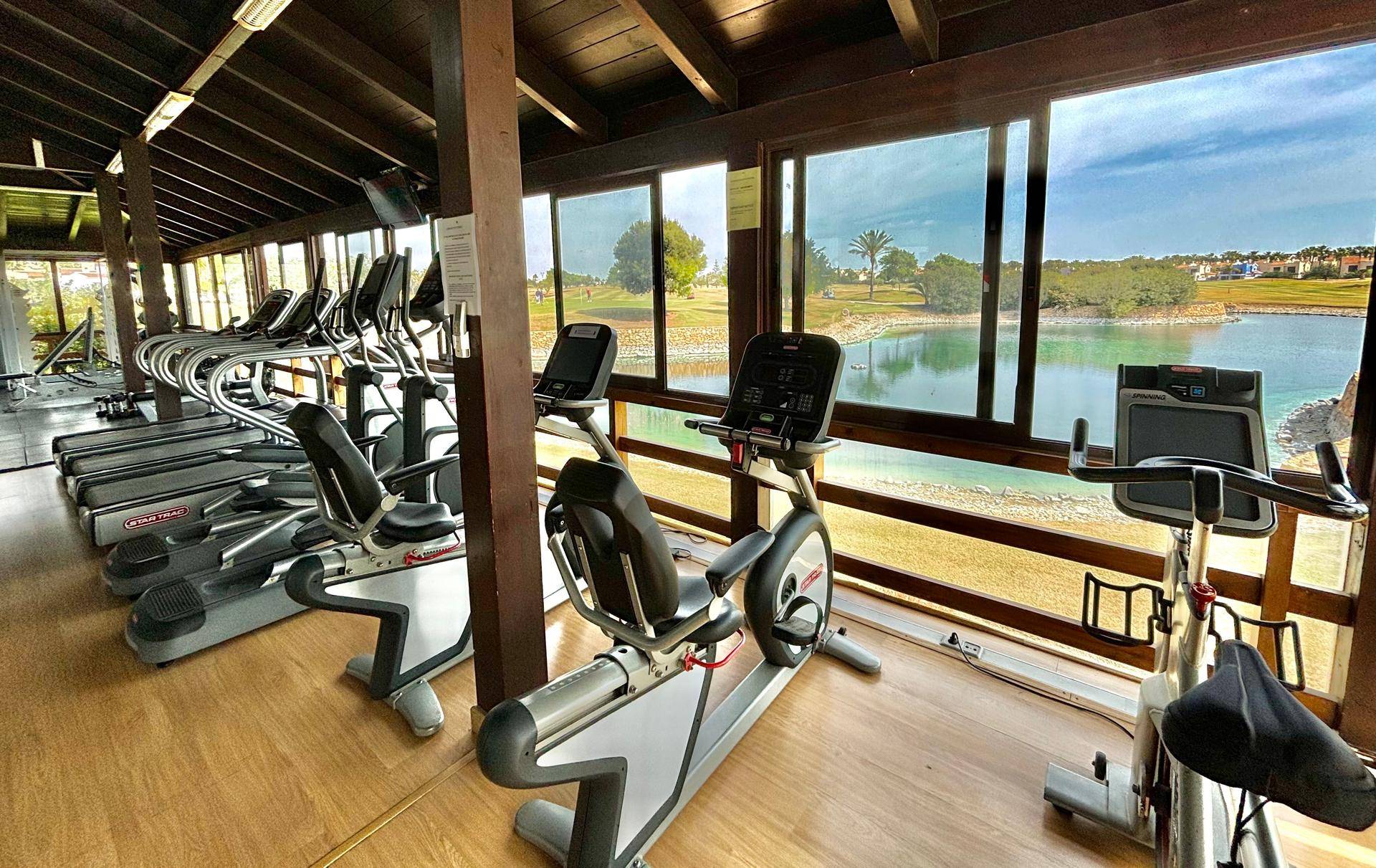 Fitnessraum mit verschiedenen Trainingsgeräten und Panoramablick auf einen See.