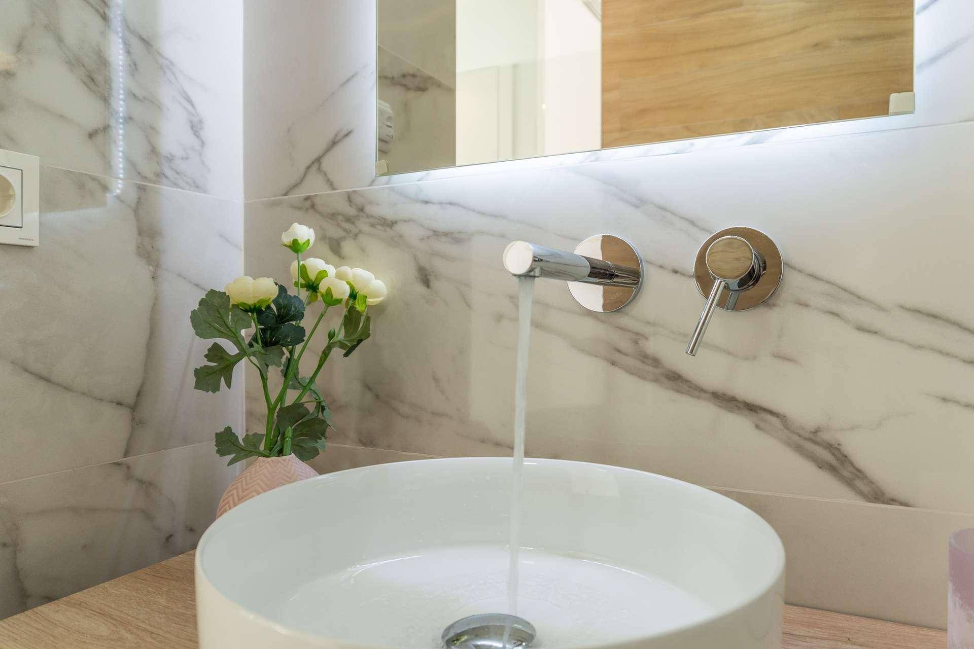 Modernes Badezimmer mit Aufsatzwaschbecken, Wandarmatur und Marmorfliesen.