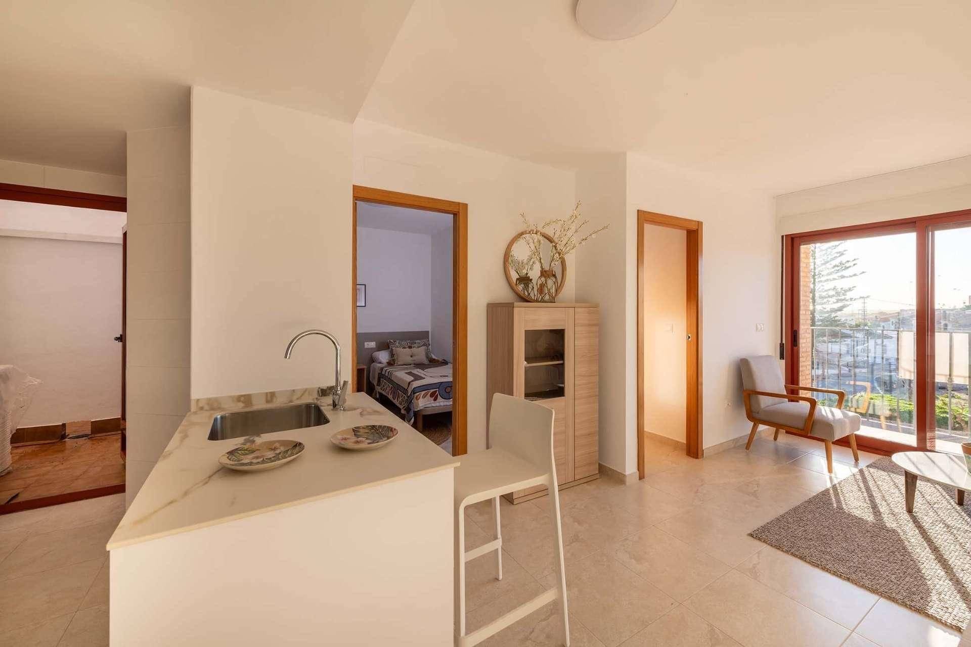 Heller offener Wohnbereich mit Kücheninsel, Esstisch und Zugang zu einem Balkon.