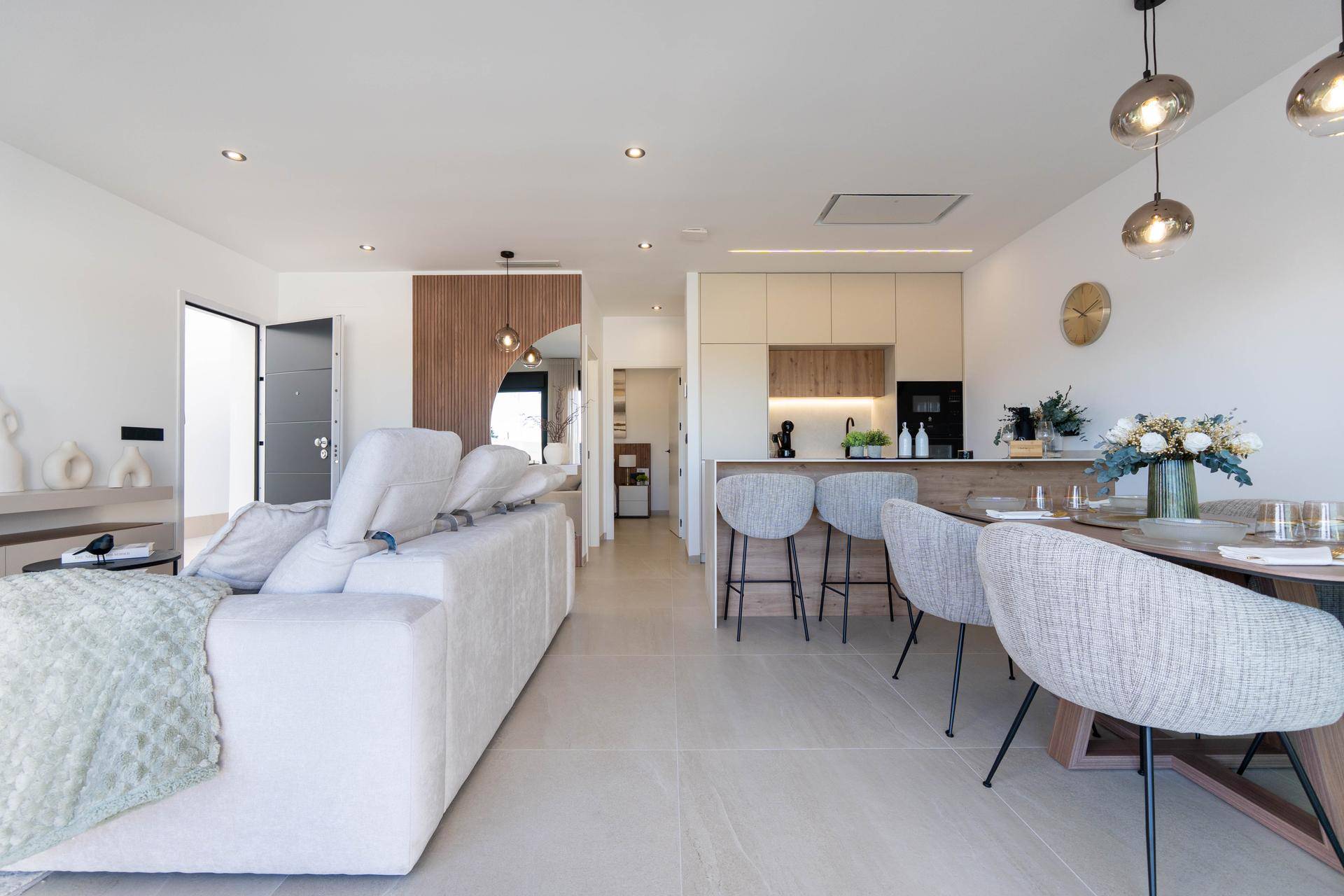 Geräumiger Wohn- und Essbereich mit offener Küche, beigem Sofa und moderner Einrichtung.