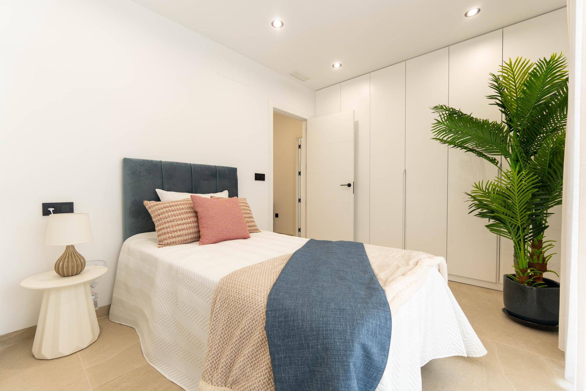 Helles Schlafzimmer mit Einzelbett, Einbauschränken und dekorativer Palme.