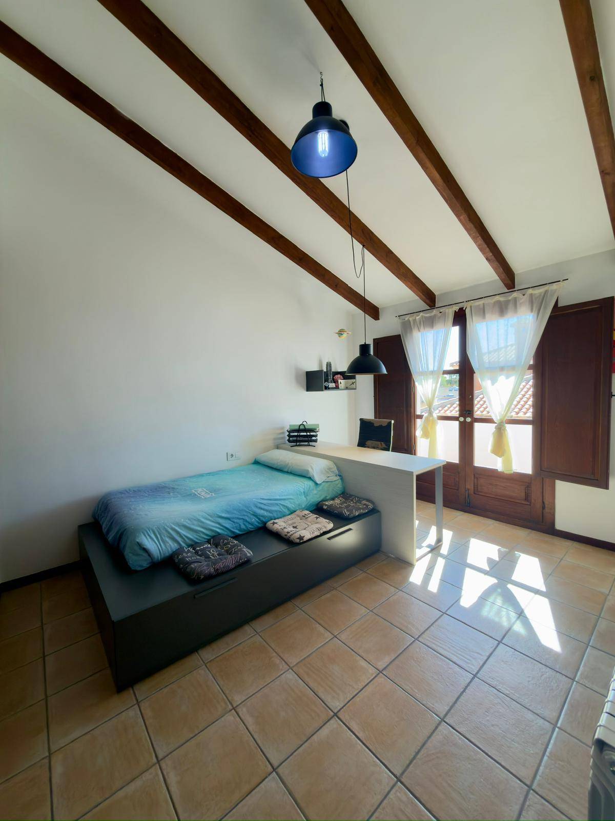 Helles Schlafzimmer mit sichtbaren Holzbalken, Einzelbett und Schreibtisch.