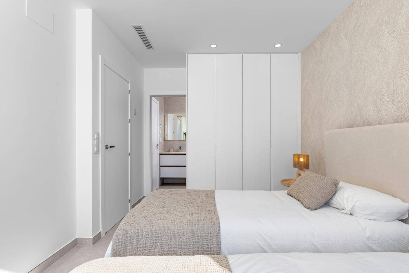 Schlafzimmer mit integriertem Kleiderschrank und direktem Zugang zu einem modernen Badezimmer.