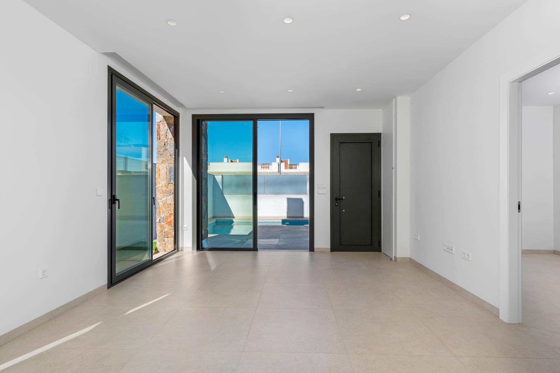 Heller, leerer Wohnbereich mit großen Schiebetüren, die auf eine Terrasse führen, und modernem Fliesenboden.