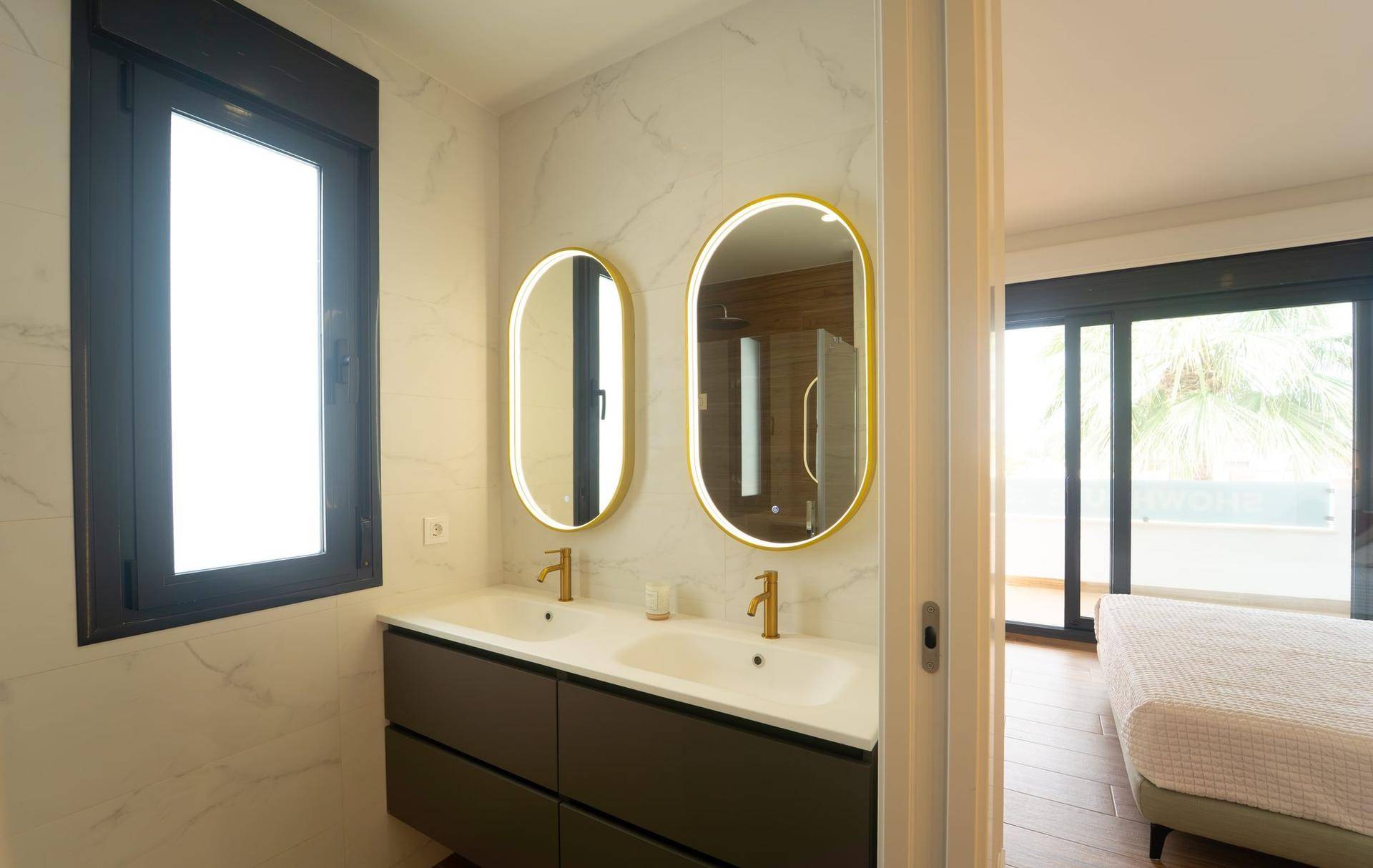 Elegantes Ensuite-Badezimmer mit Doppelwaschbecken, beleuchteten Spiegeln und Zugang zum Schlafzimmer.