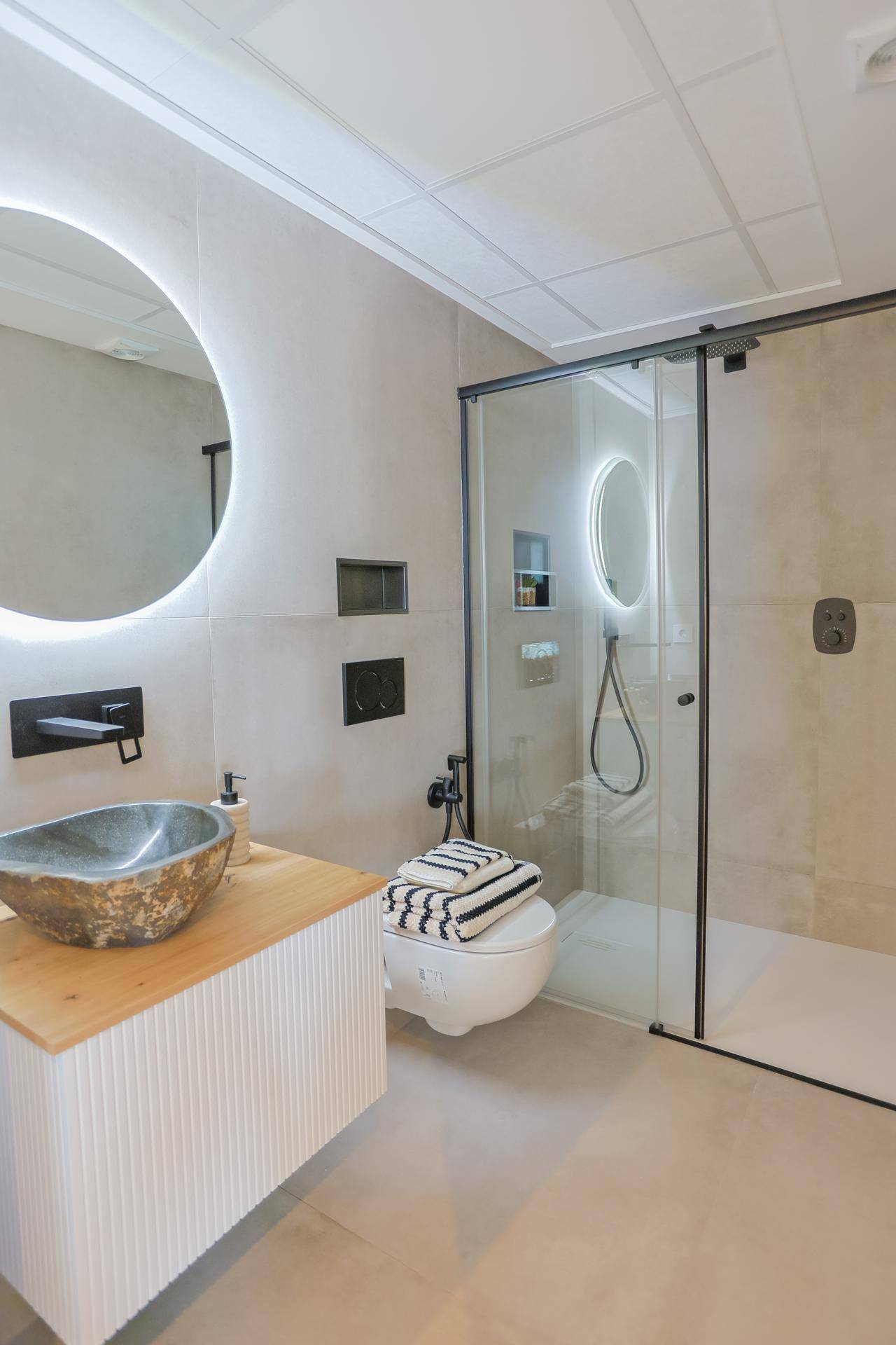 Elegantes Badezimmer mit modernem Waschbecken, runden Spiegel und begehbarer Dusche.