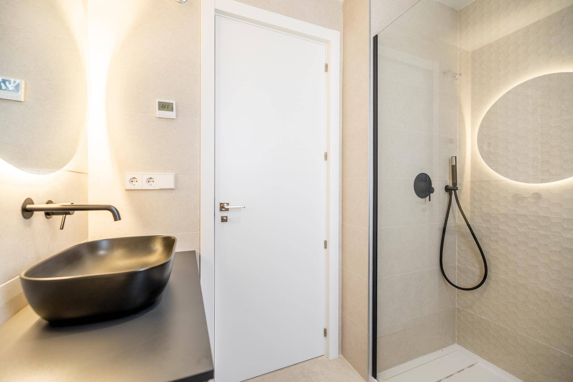 Modernes Badezimmer mit schwarzem Waschbecken, beleuchtetem Spiegel und ebenerdiger Dusche.