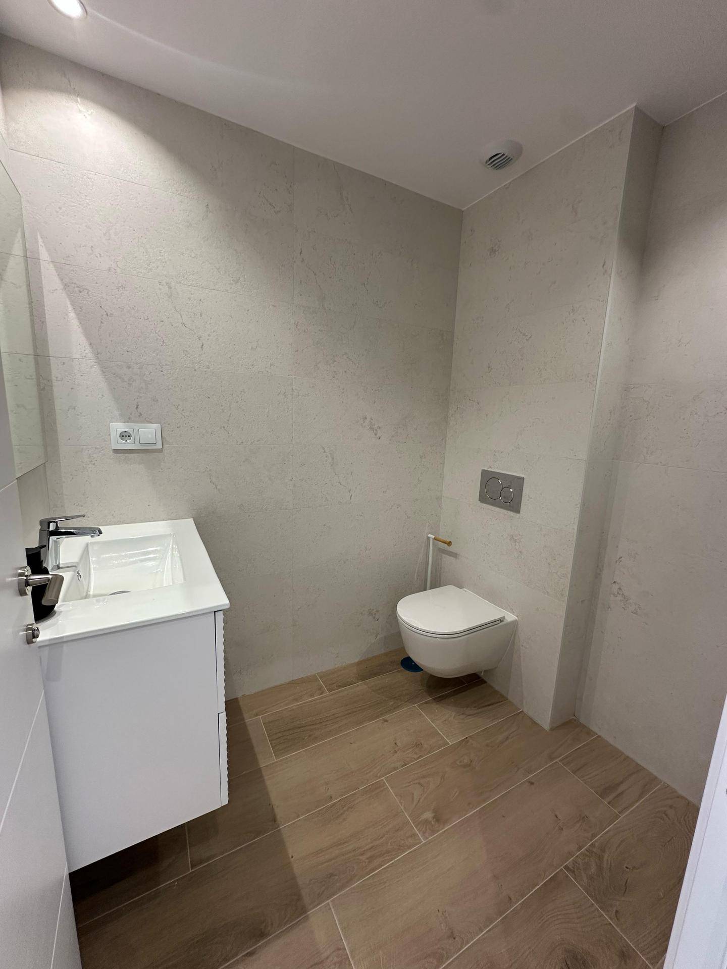 Helles Badezimmer mit wandhängendem WC, modernem Waschtisch und Fliesenboden.