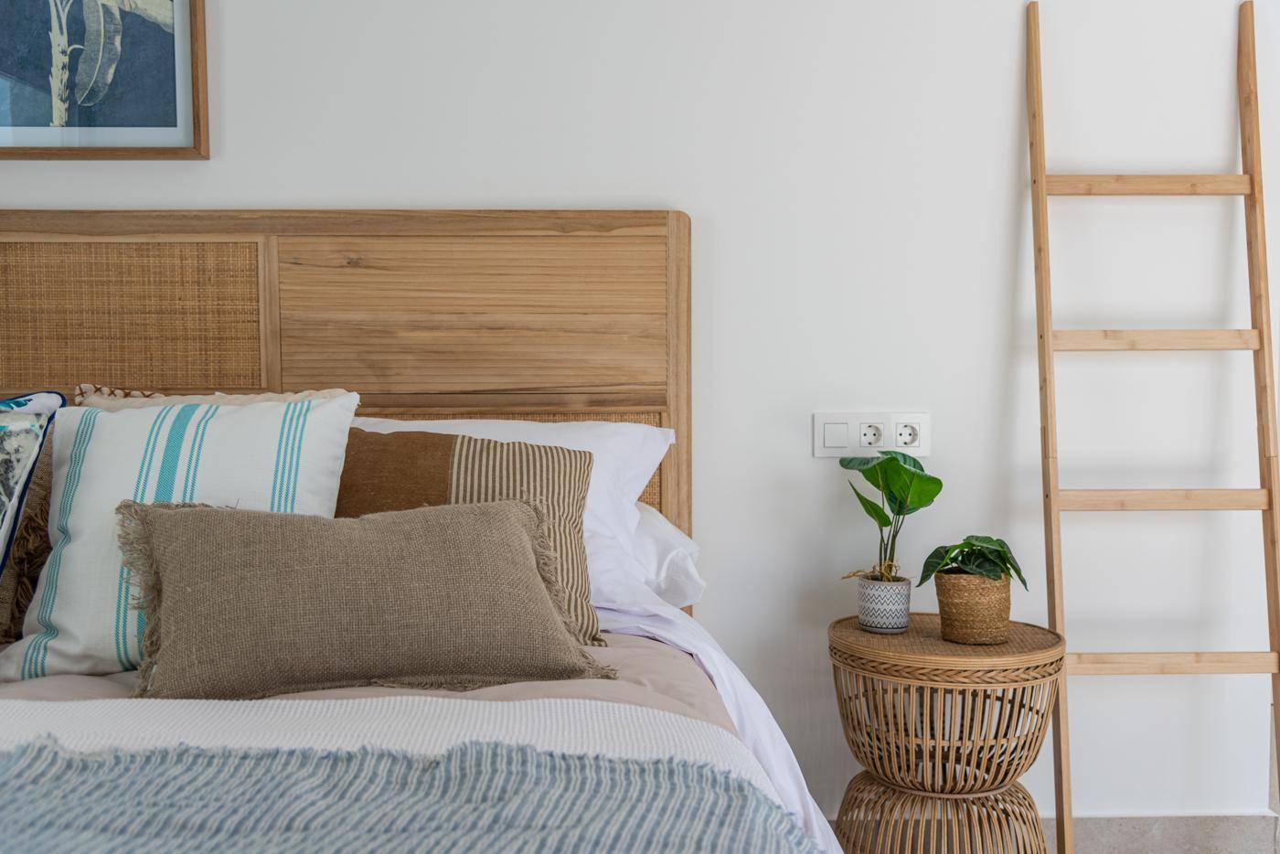 Gemütliches Schlafzimmer mit Holzkopfteil, Rattan-Nachttisch und Pflanzen.
