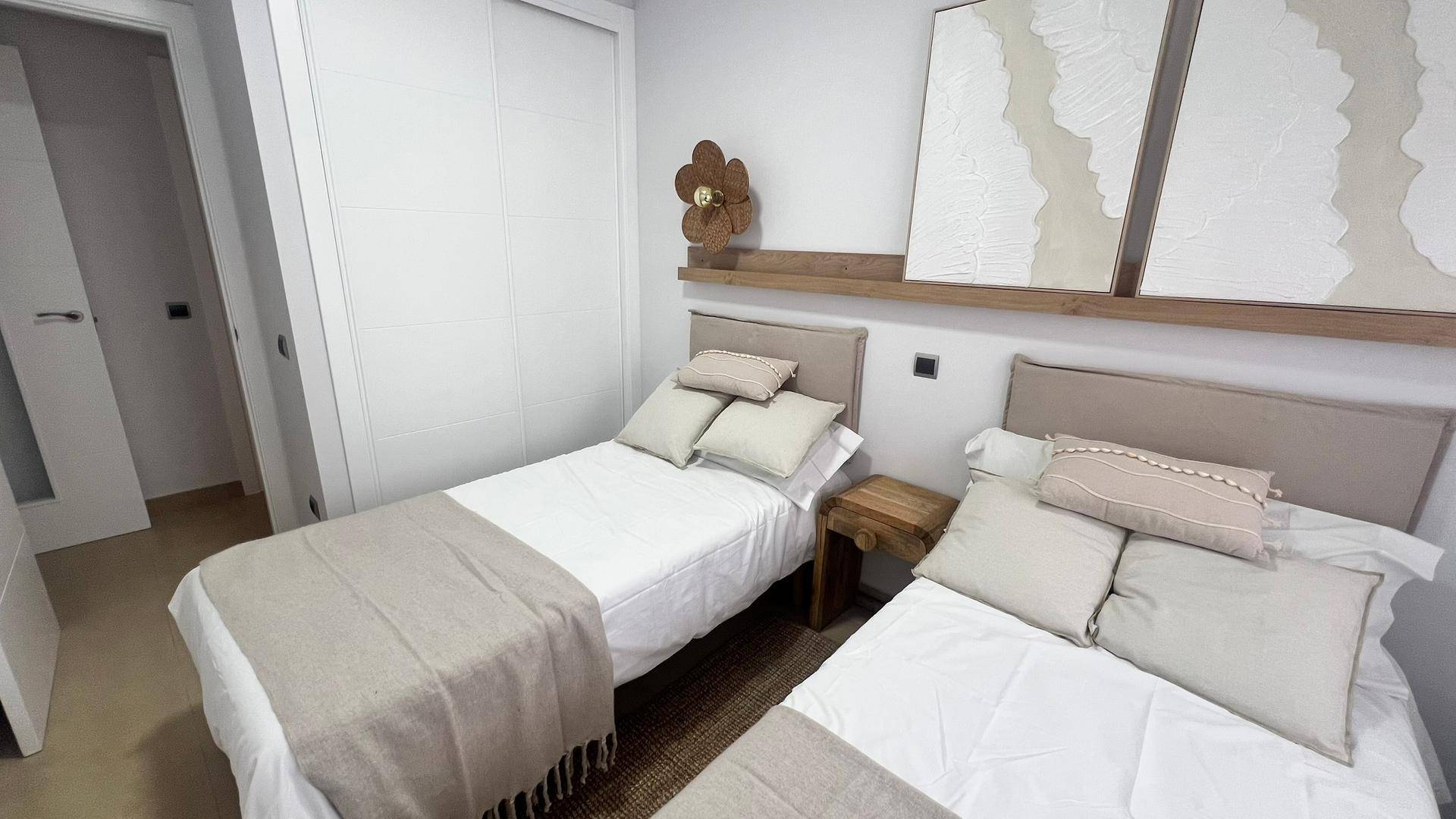 Helles Schlafzimmer mit zwei Einzelbetten, Einbauschrank und moderner Wanddekoration.