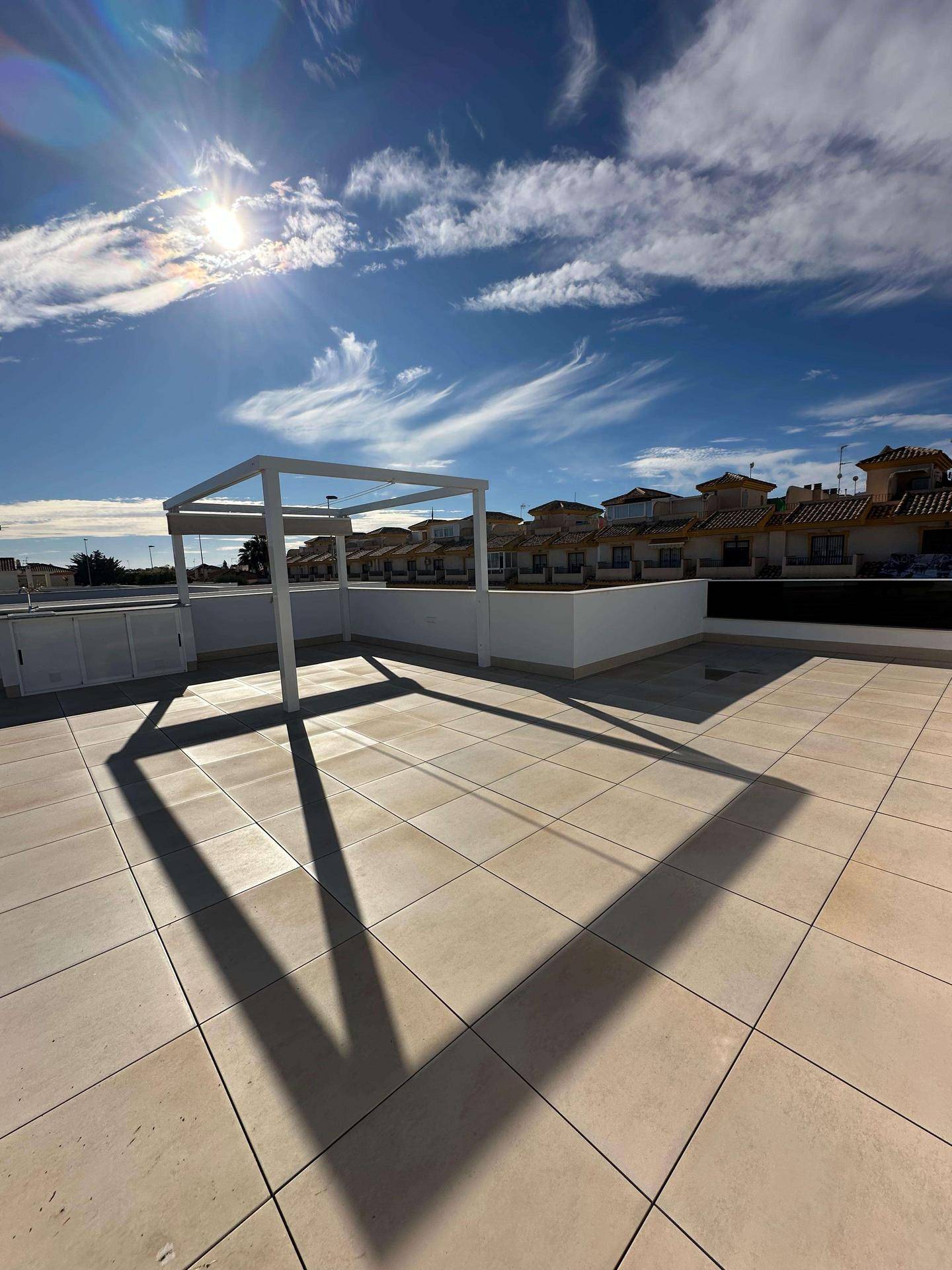 Geräumige Dachterrasse mit Fliesenboden und Pergola-Struktur unter blauem Himmel.