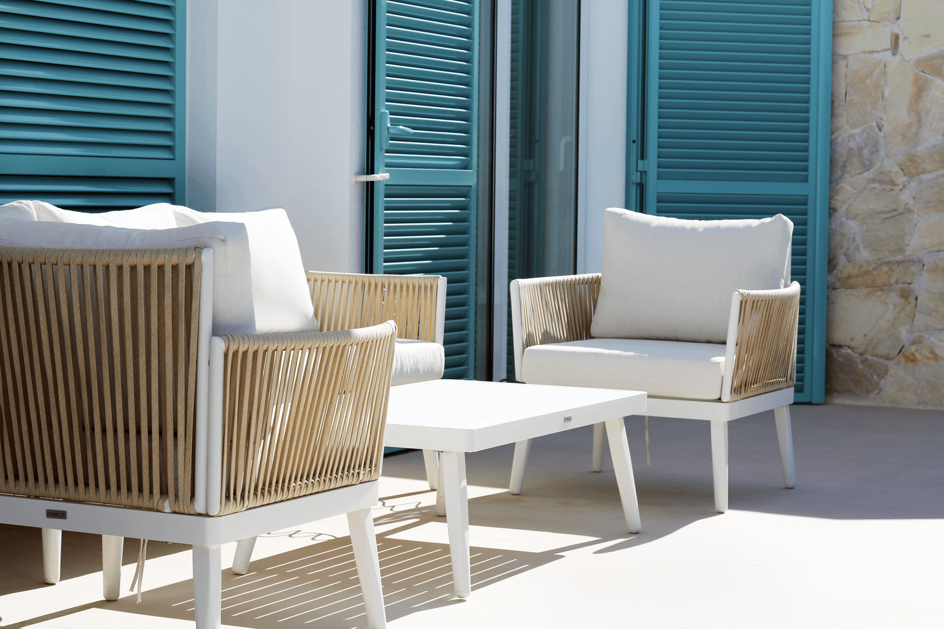 Gemütliche Lounge-Möbel auf der Terrasse mit türkisfarbenen Fensterläden im Hintergrund.