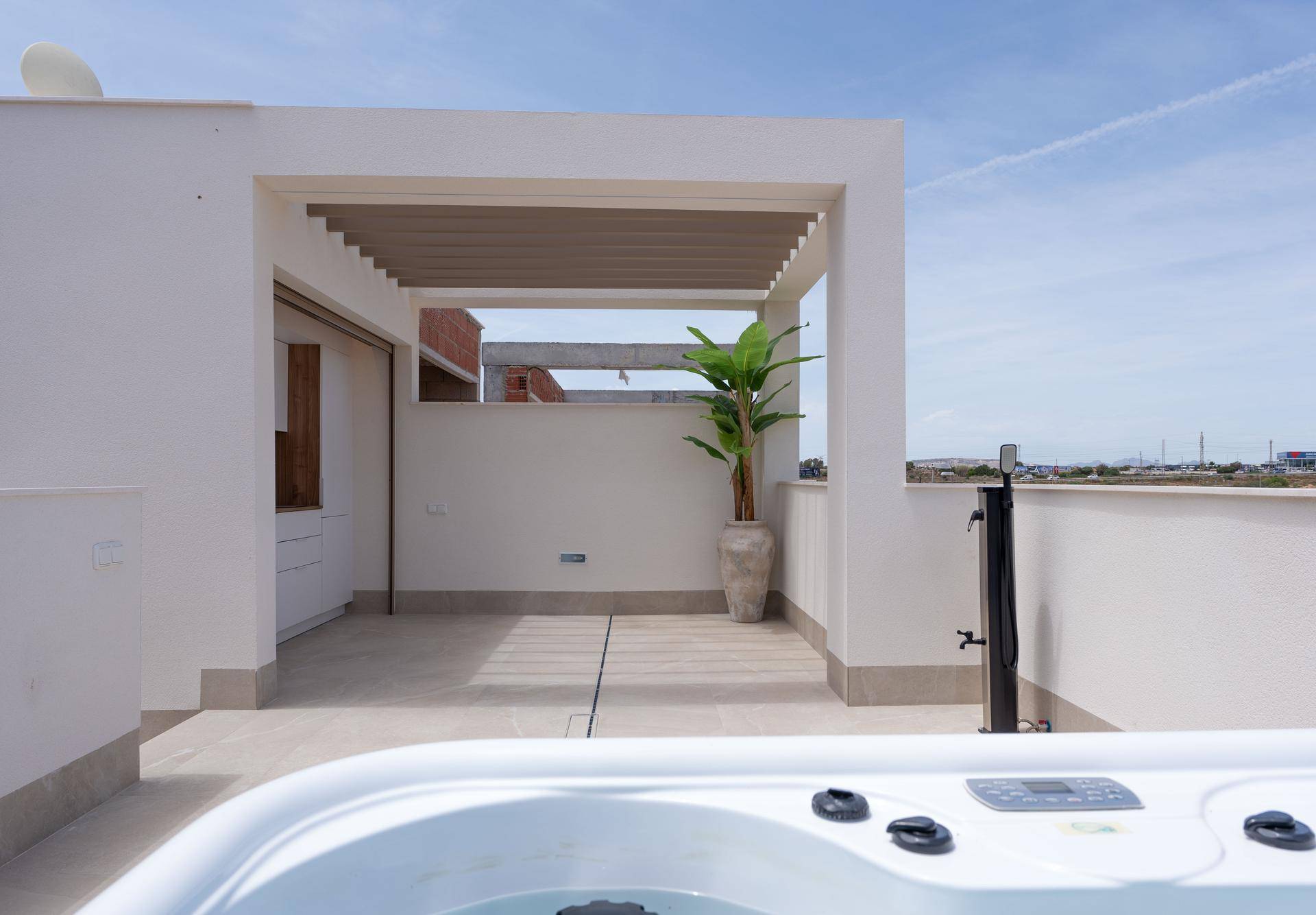Dachterrasse mit Whirlpool und Pergola, die Schatten spendet, unter blauem Himmel.