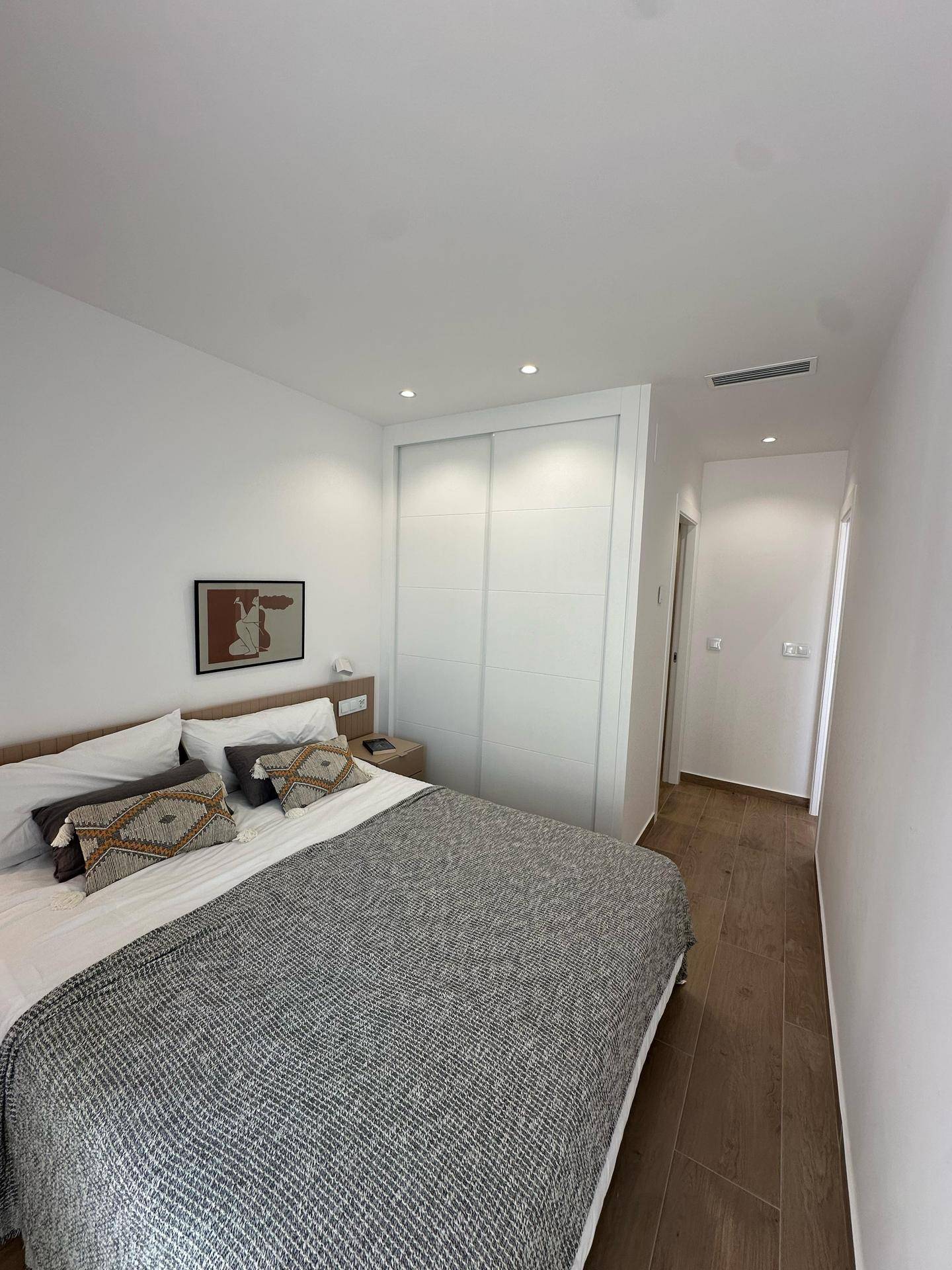 Modernes Schlafzimmer mit Doppelbett, integriertem Kleiderschrank und Holzoptik-Fliesenboden.