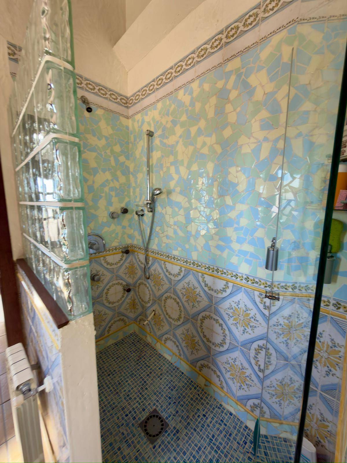 Duschbereich mit farbenfrohen Mosaikfliesen und Glasbausteinwand.