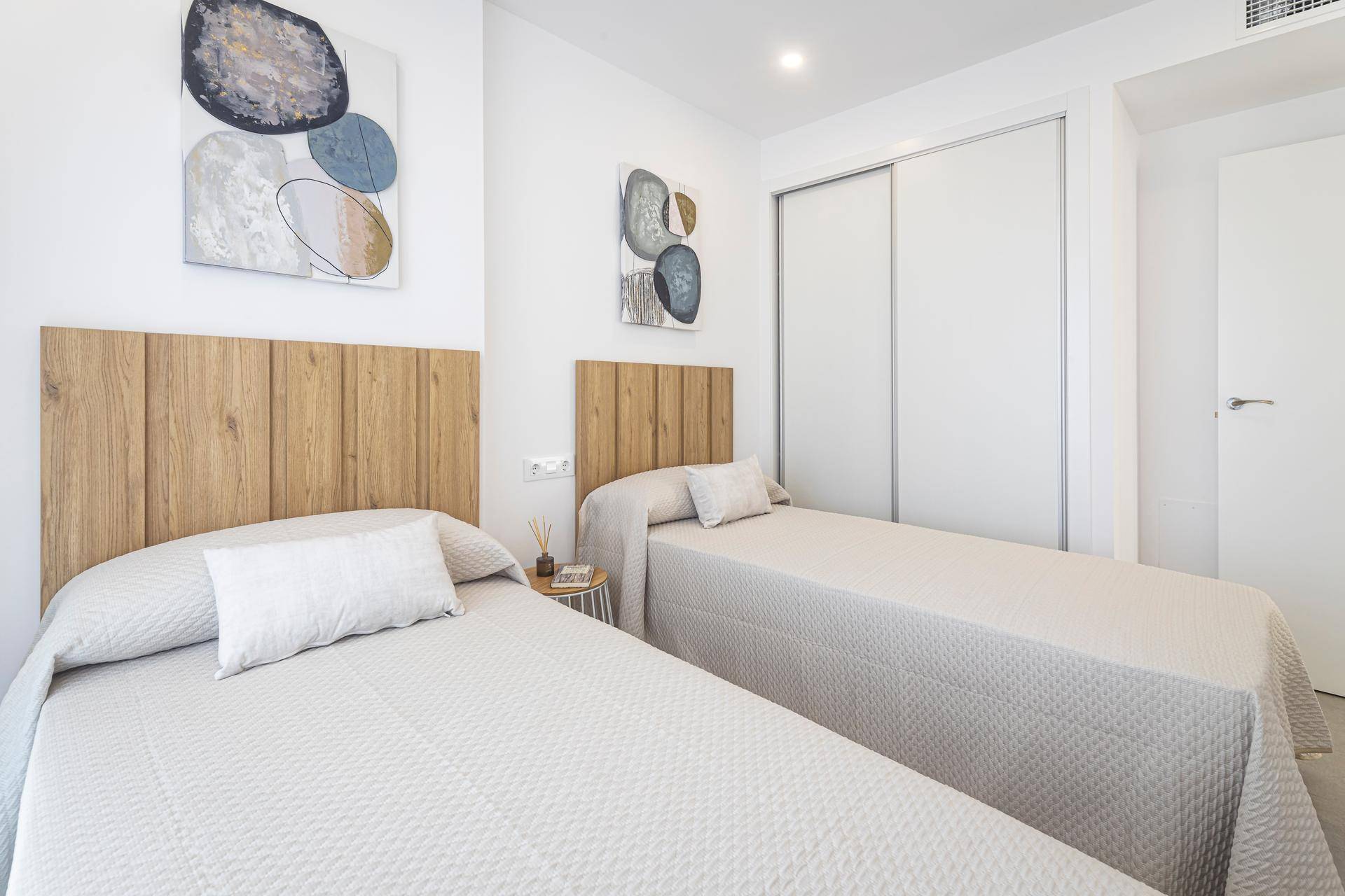 Helles Schlafzimmer mit zwei Einzelbetten, Holz-Kopfteilen und Einbauschränken.