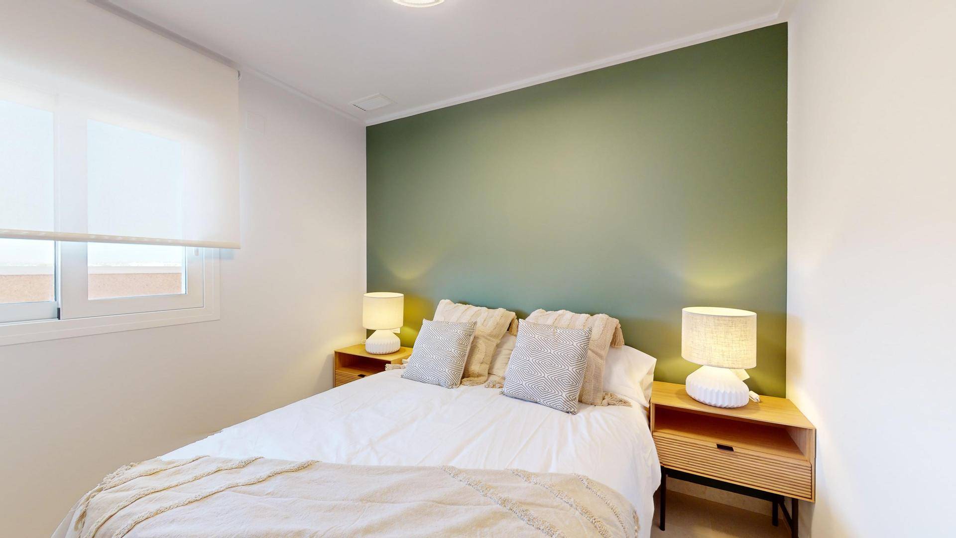 Helles Schlafzimmer mit Doppelbett, grüner Akzentwand und Fenster mit Rollo.