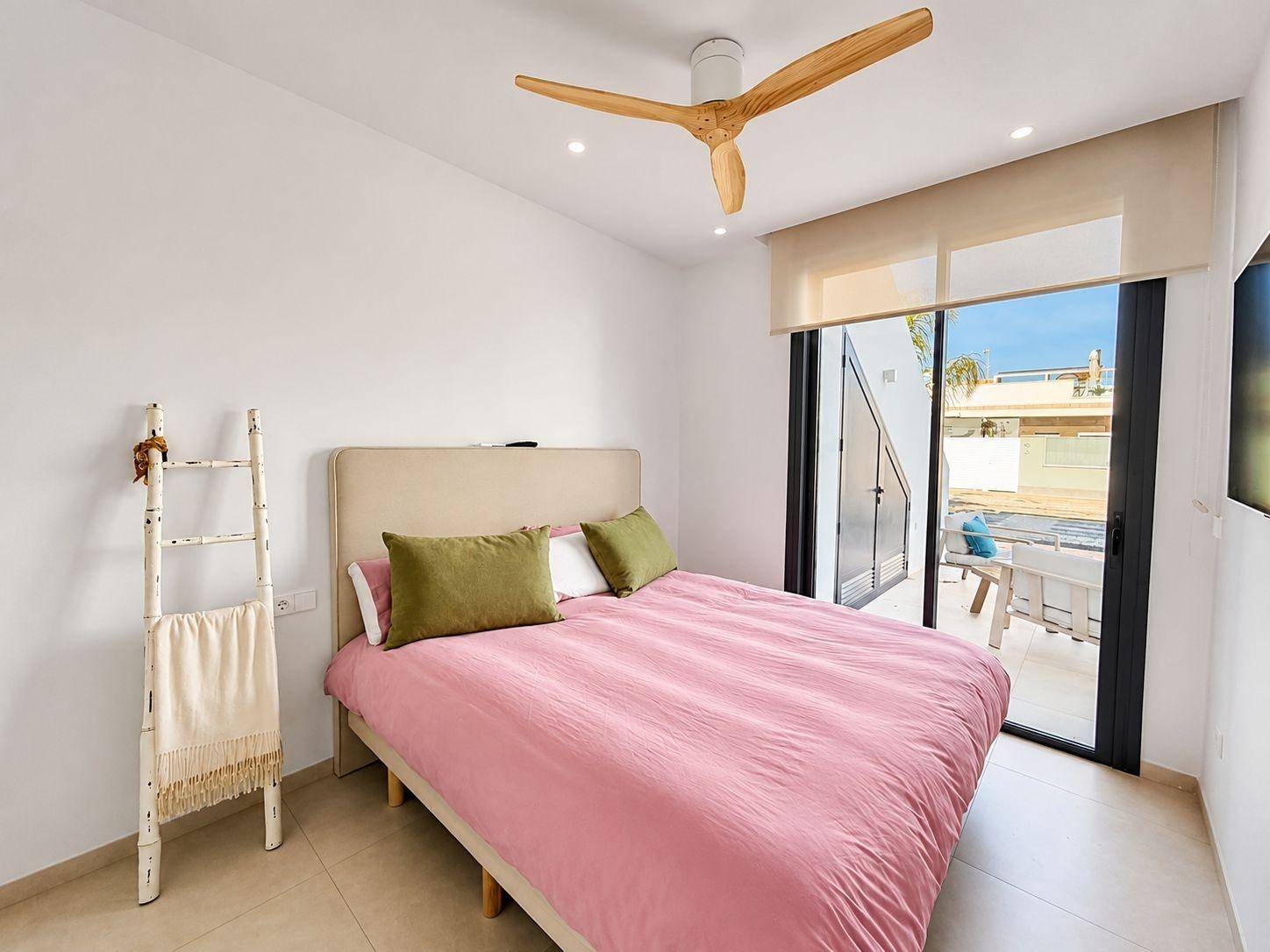 Gemütliches Schlafzimmer mit rosa Bettwäsche, Deckenventilator und Blick auf den Außenbereich.